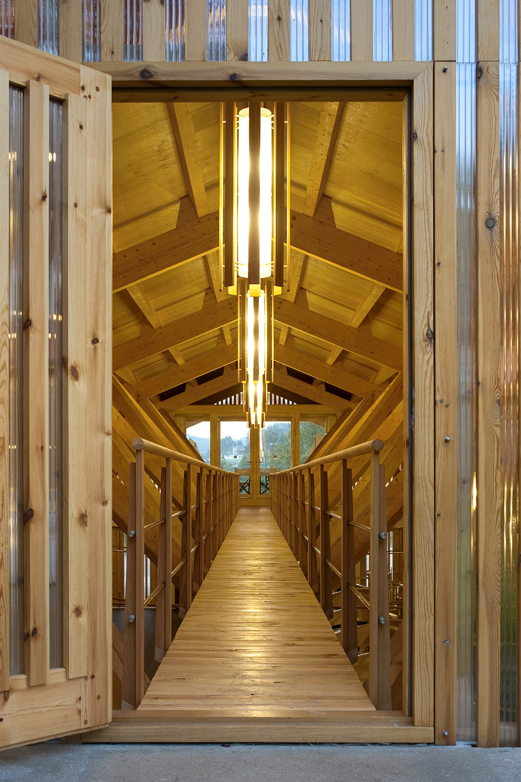 Timber footbridge with exposed truss ceiling and vertical light slot framing the landscape beyond