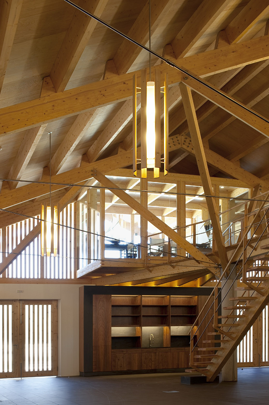 Double-height interior with diagonal timber trusses and a pendant light fixture above a wooden cabinetry unit