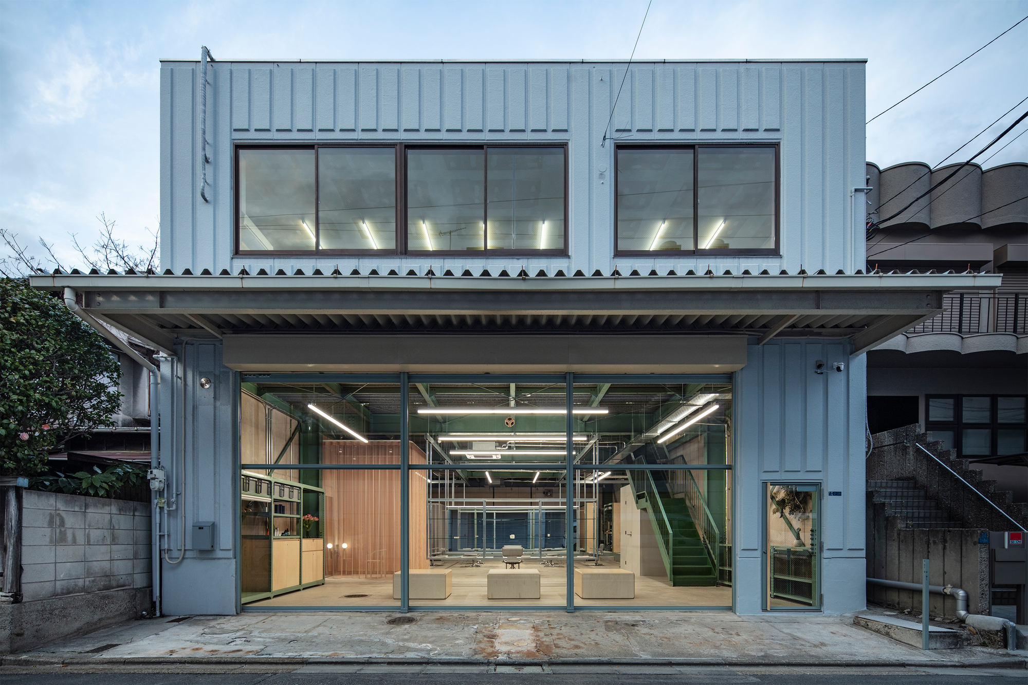 Street facade with corrugated metal cladding and fully open ground floor revealing interior under dusk light