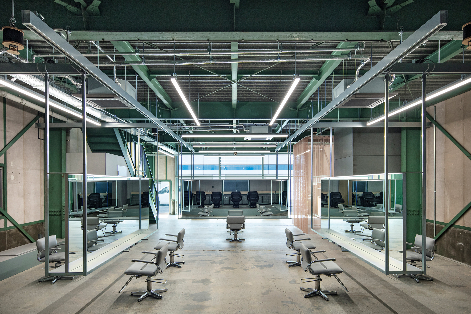 Open salon floor with rows of styling chairs under exposed green steel structure and linear lighting