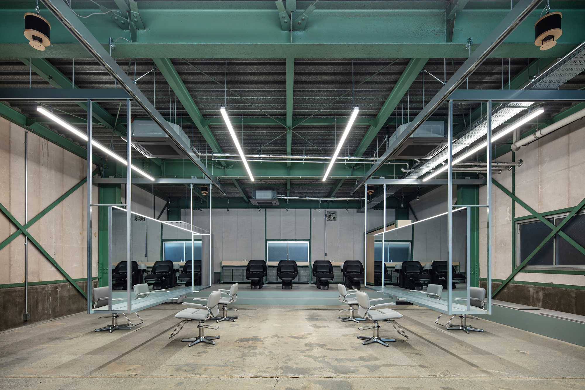 Interior salon with exposed green steel trusses and linear fluorescent lighting above white styling chairs
