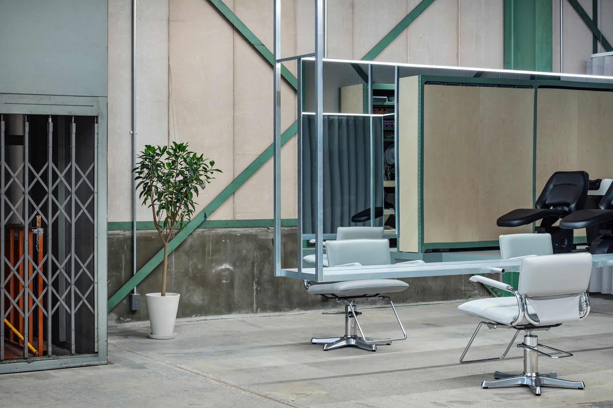Two styling chairs on polished concrete floor beside a folding metal gate and potted plant