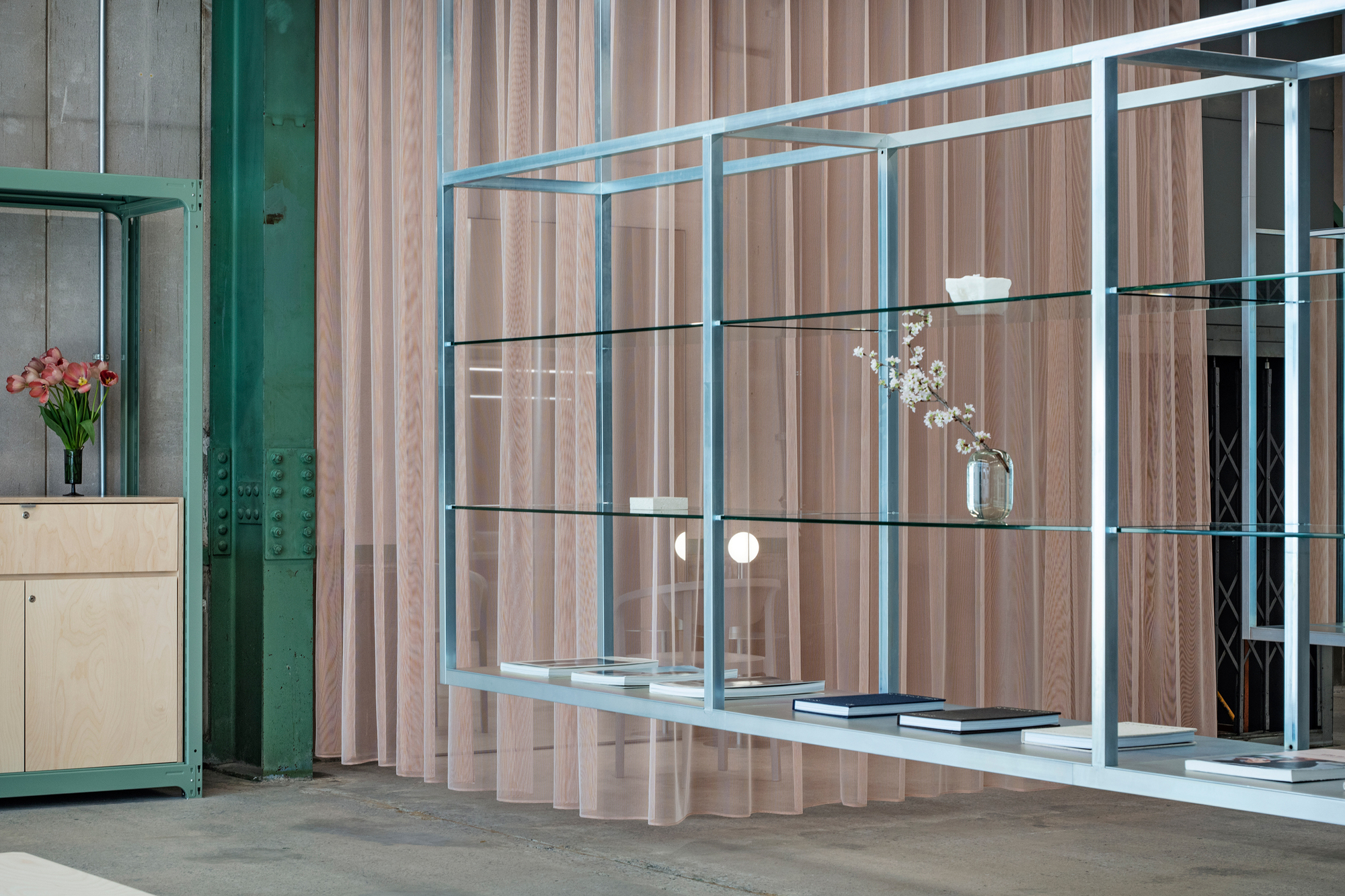 Glass shelving unit with flowers and books against a ribbed timber screen beside a green column