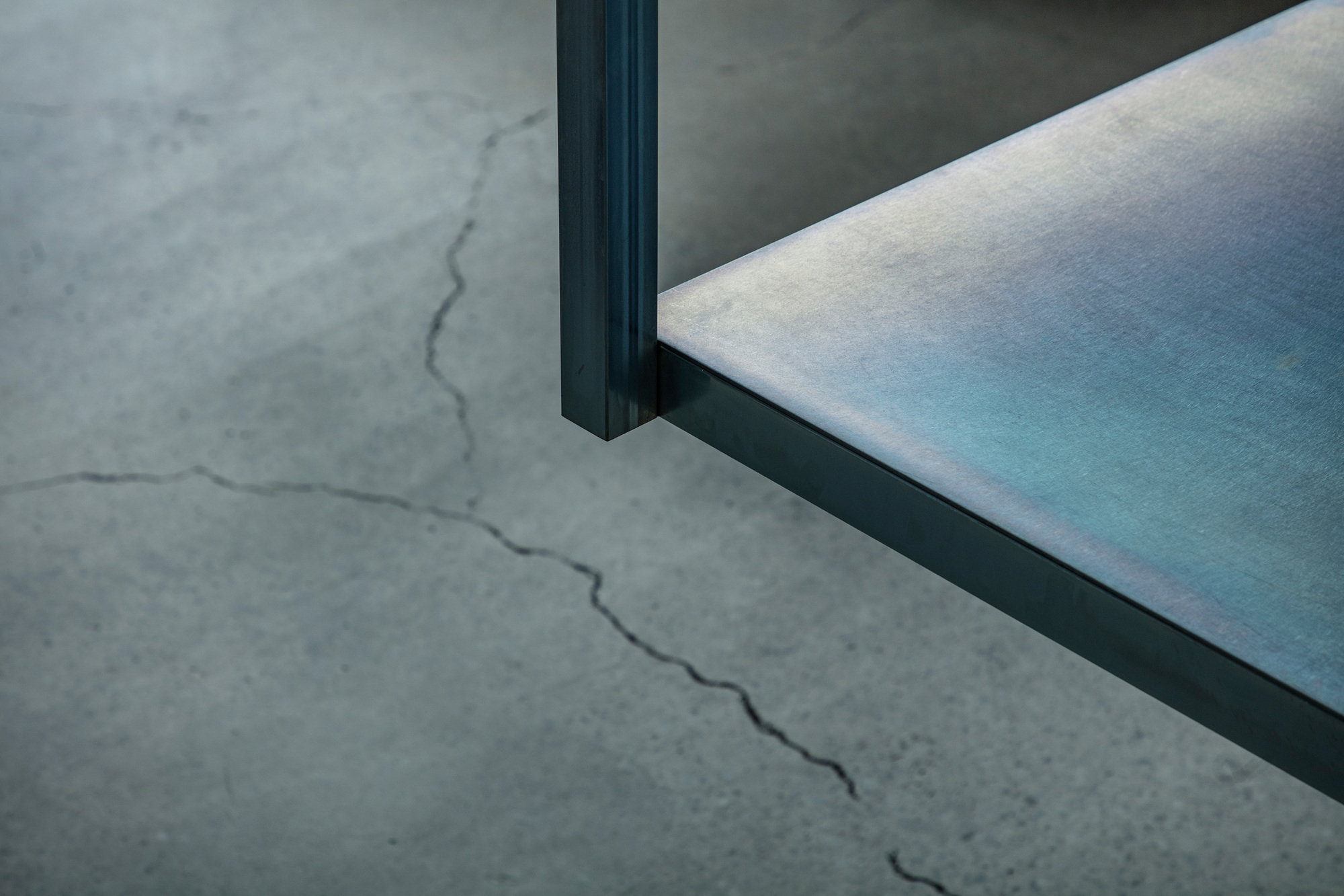 Detail of dark steel frame meeting polished floor surface with visible crack in concrete