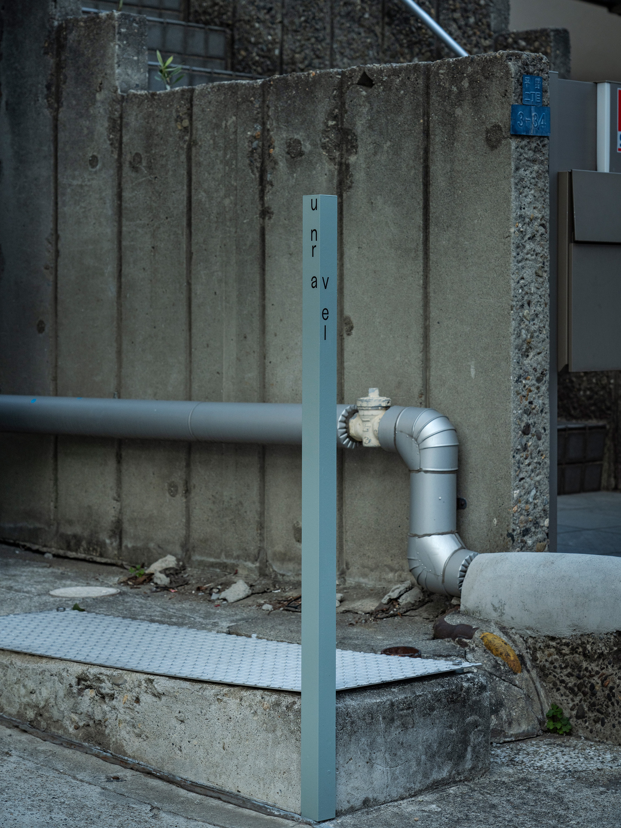Blue painted steel post with exposed plumbing pipe against board-formed concrete wall with debris