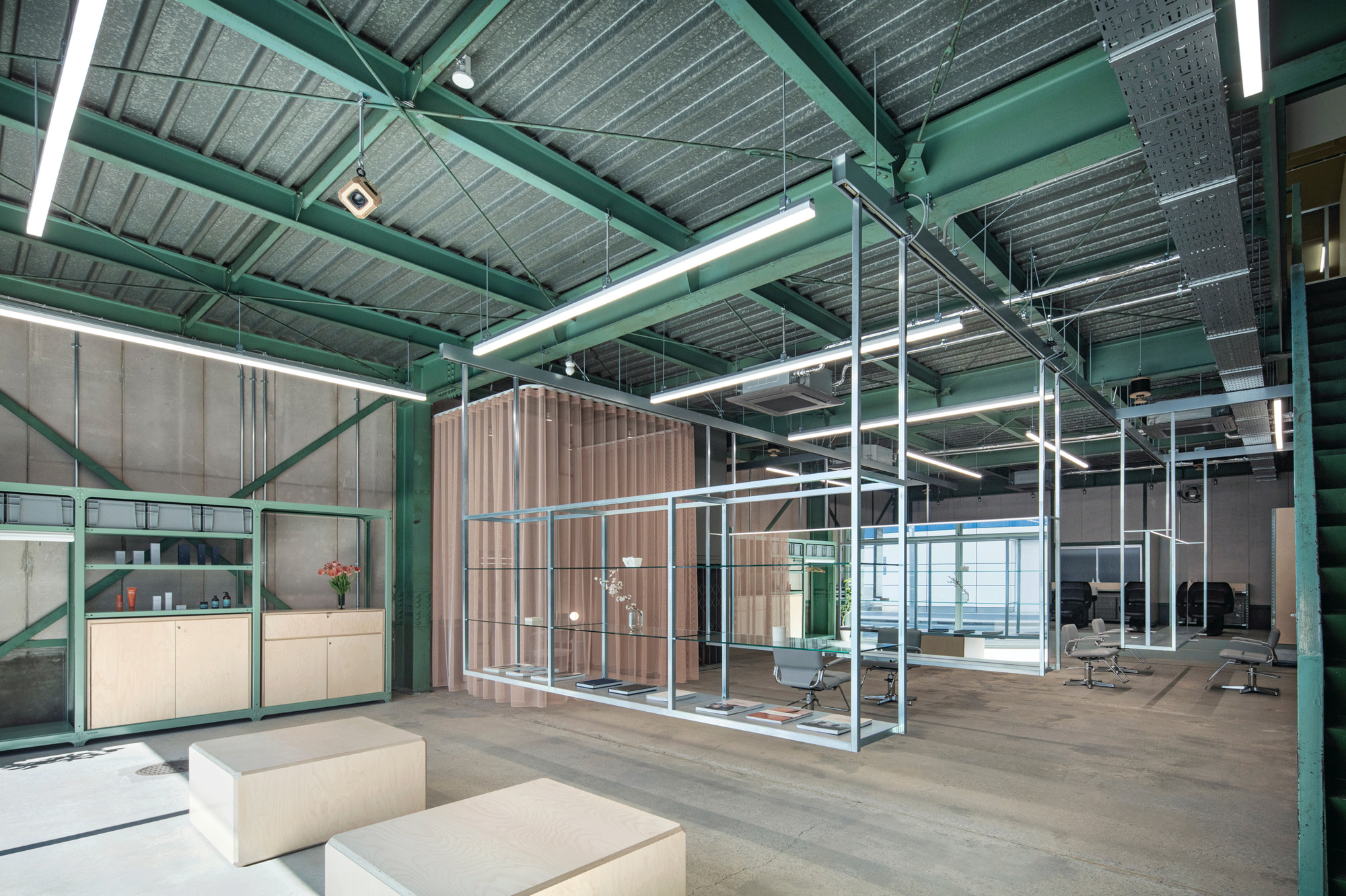 Open office interior with exposed green steel structure, corrugated slatted partitions and polished concrete flooring