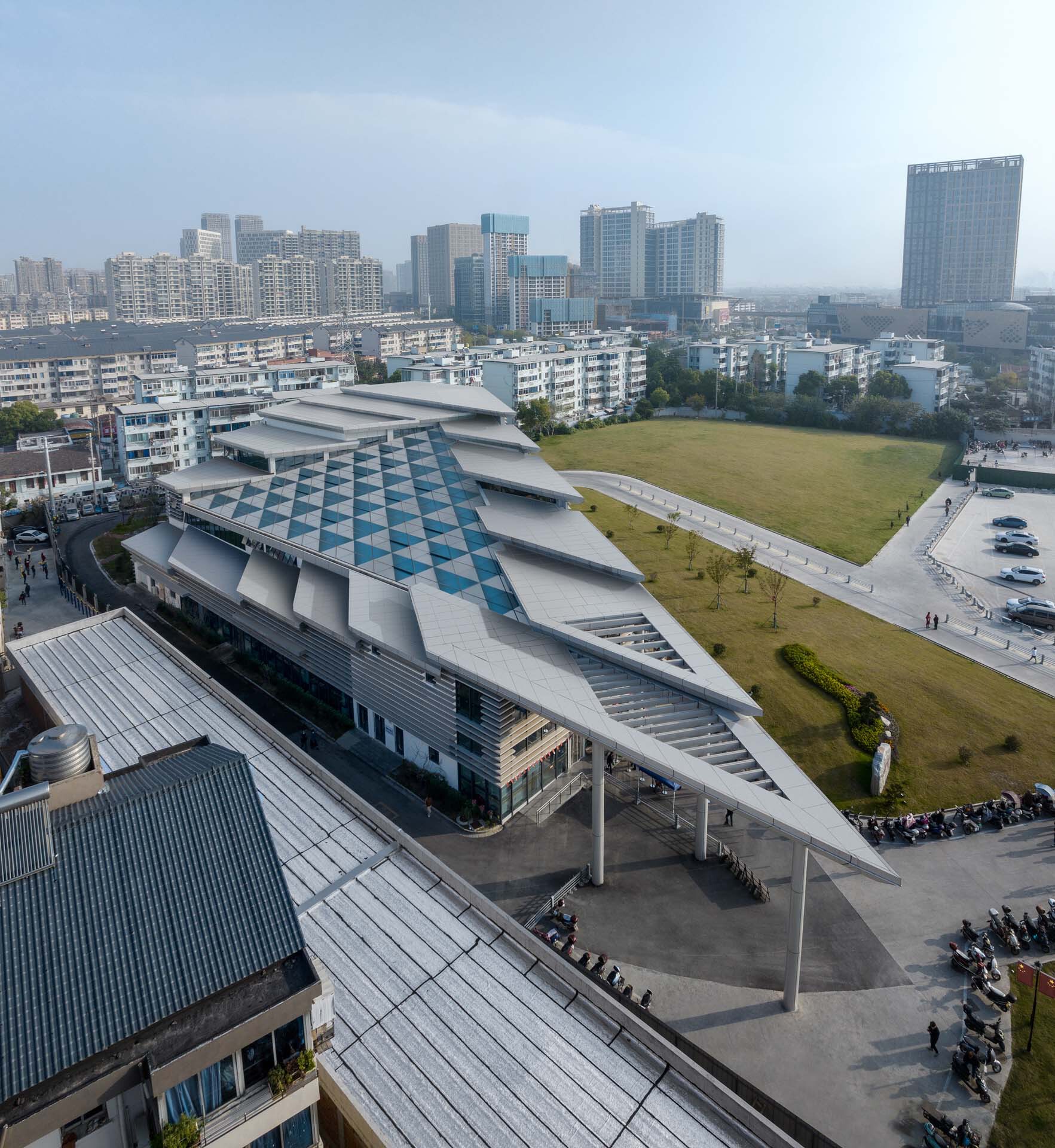 Angled aerial showing the layered roof planes and triangular canopy sheltering the entry plaza with pedestrians