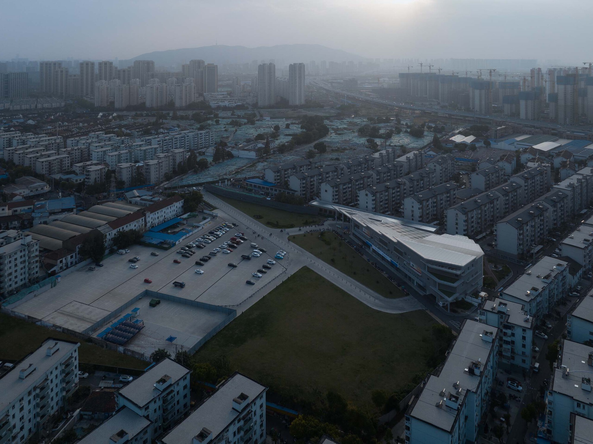 Drone view of the curved white roof among low-rise residential blocks in foggy morning light