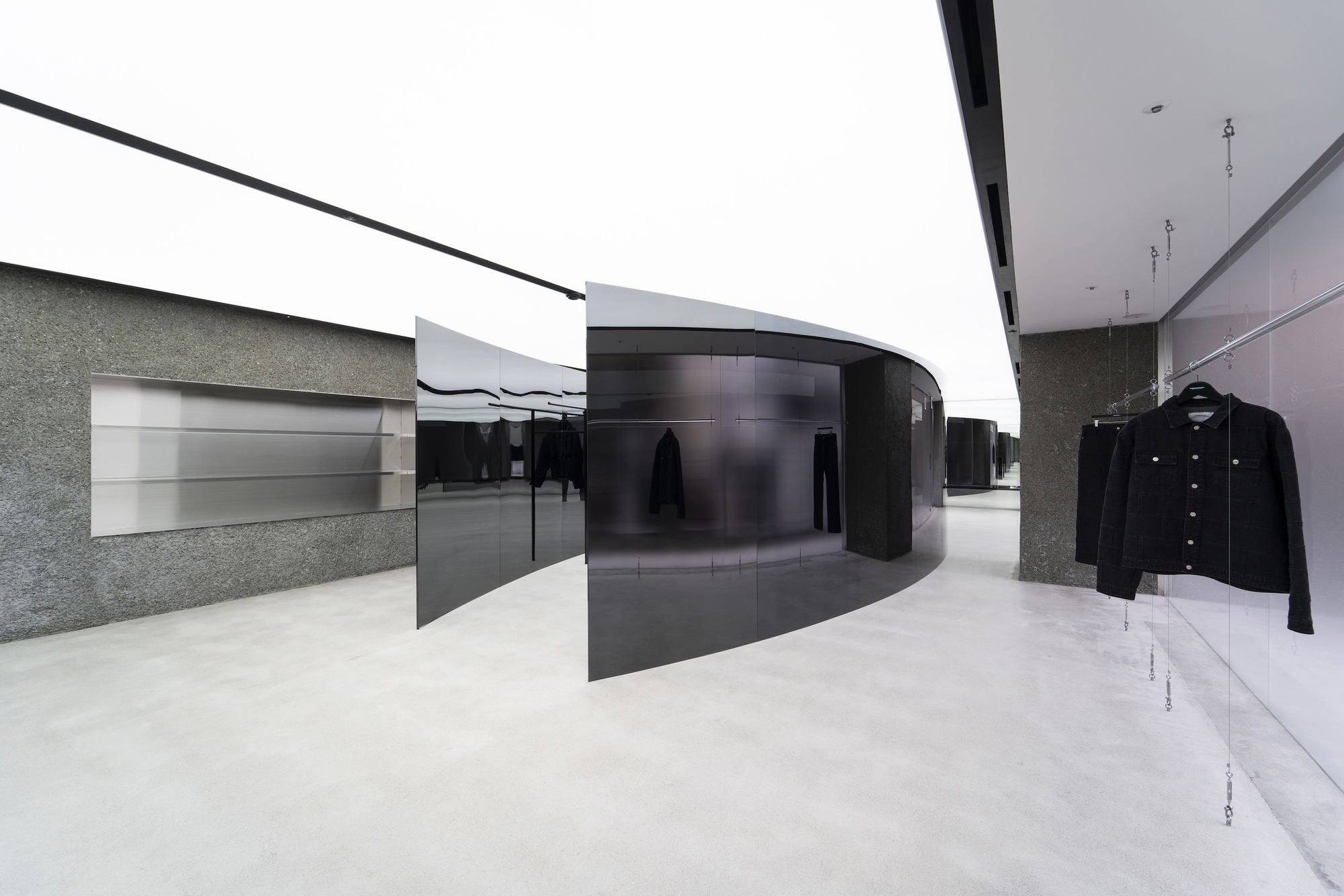 Retail interior with black curved partition walls and textured stone surfaces under a continuous skylight