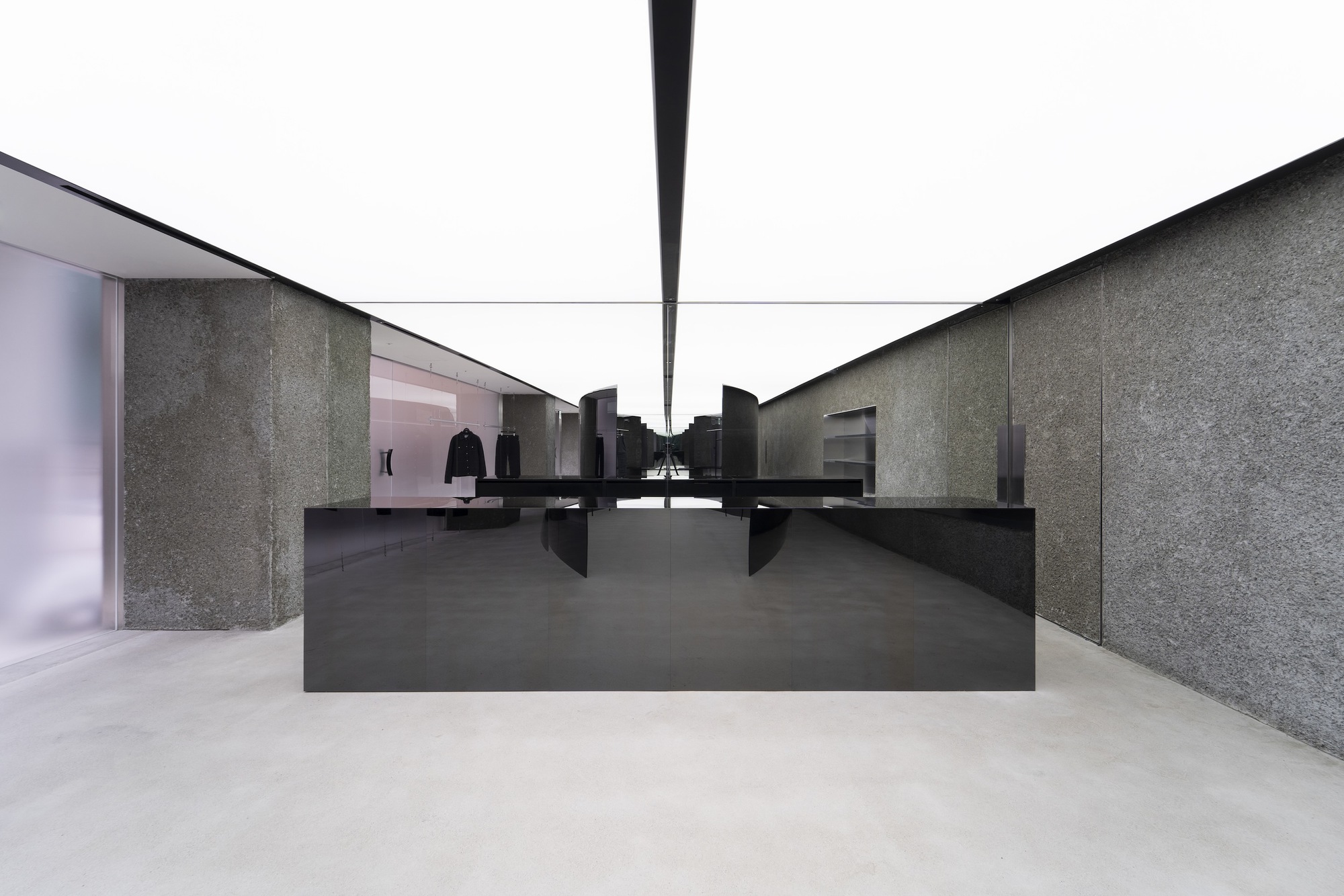 Black steel counter centered between textured stone walls and translucent glass partitions in a daylit gallery
