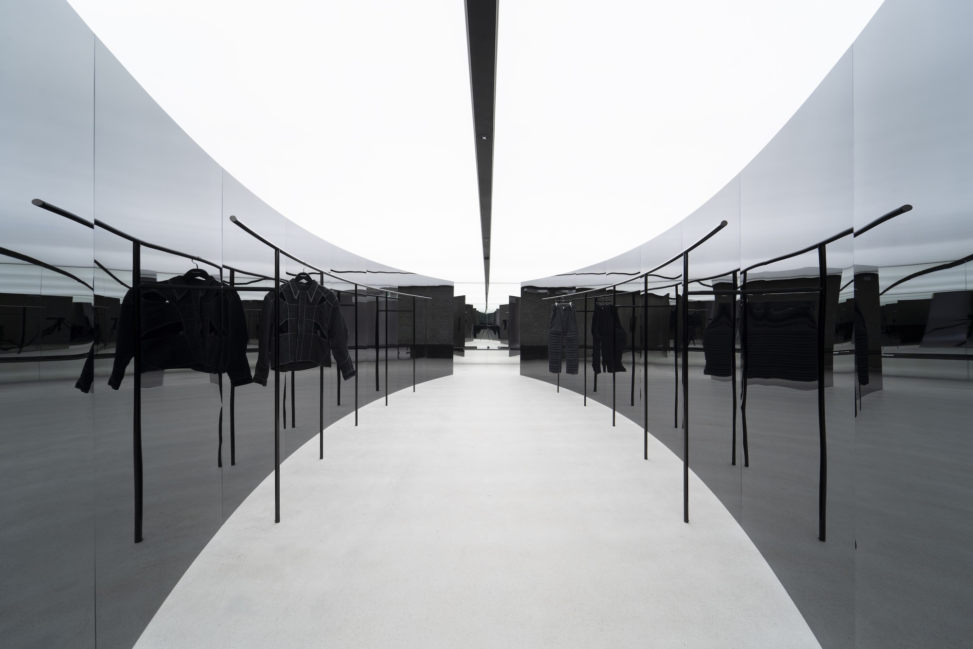 Symmetrical corridor with black metal garment racks reflected in polished floor under twin curved ceiling vaults