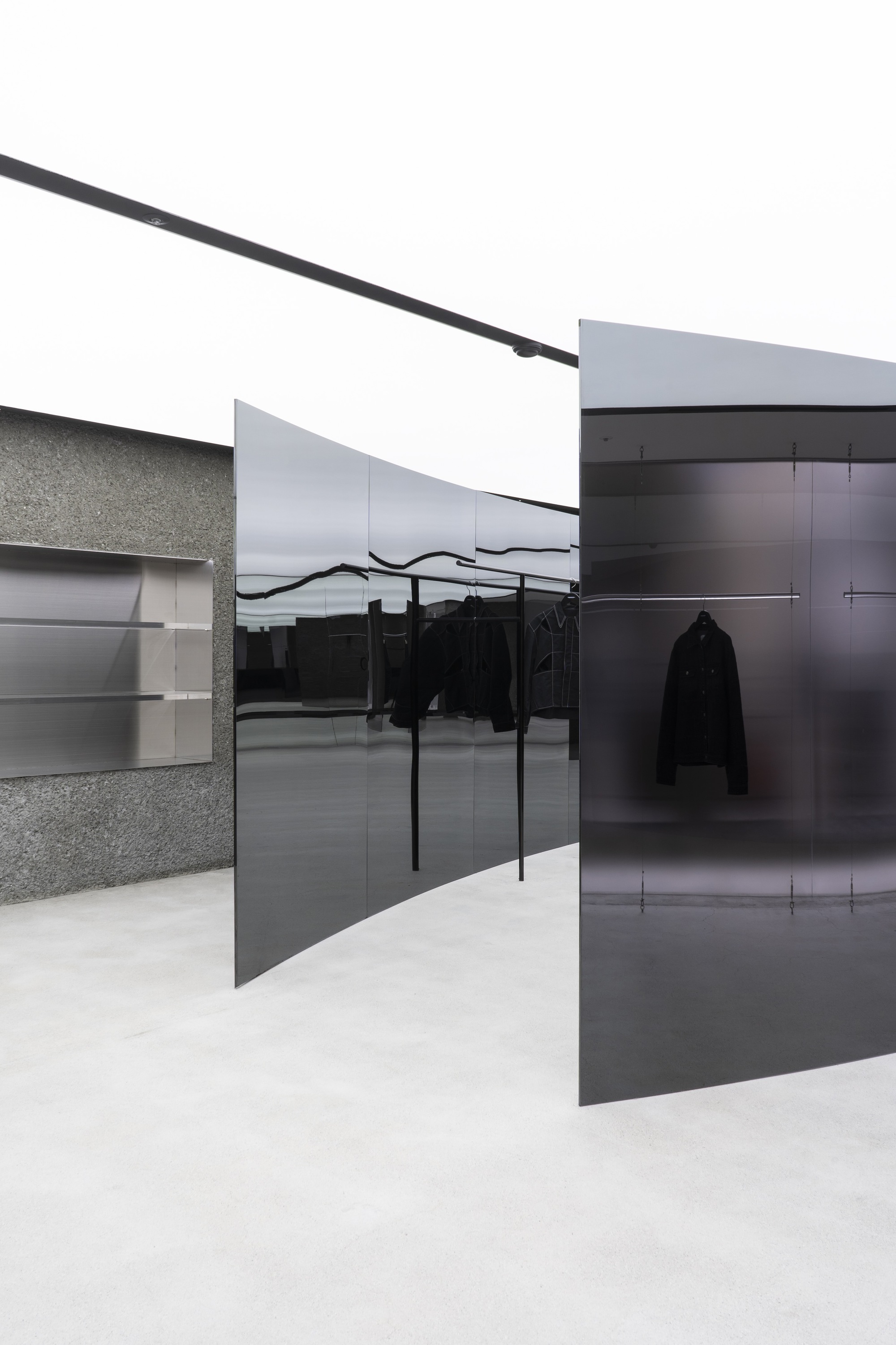 Retail interior with black glass partitions, terrazzo walls, and clothing racks under white painted ceiling