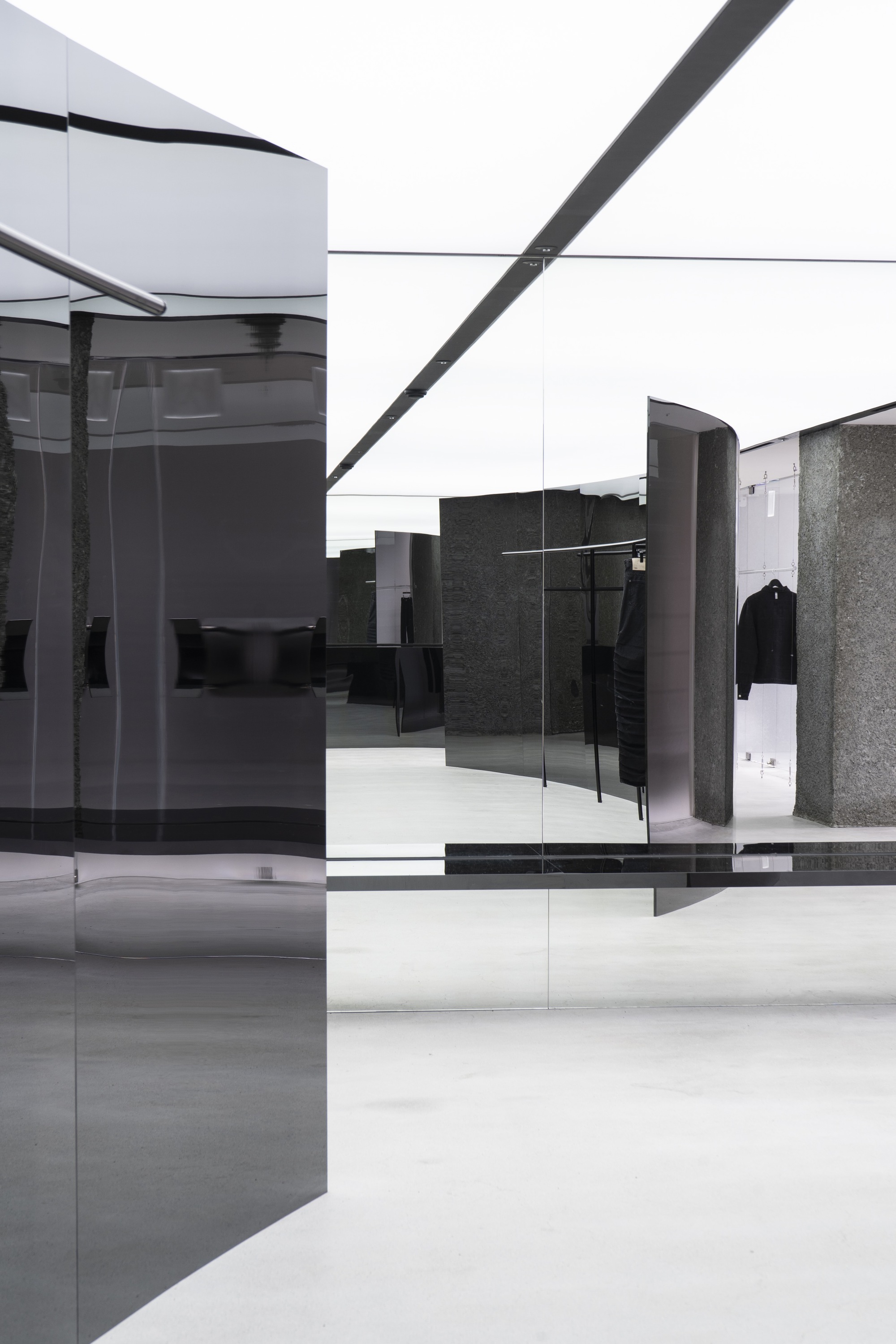 Open sales floor showing layered glass panels, curved dark metal displays, and polished terrazzo columns