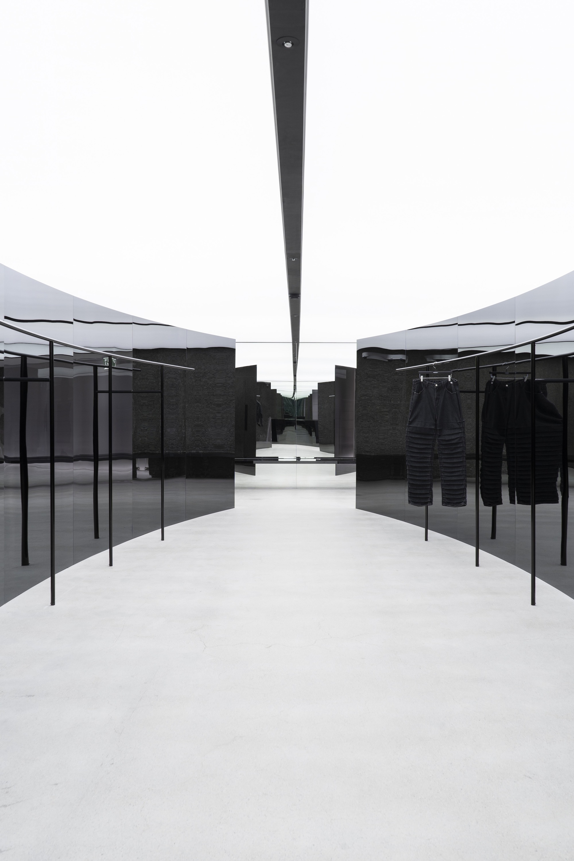 Central aisle framed by black metal garment racks beneath linear skylight slot in white ceiling