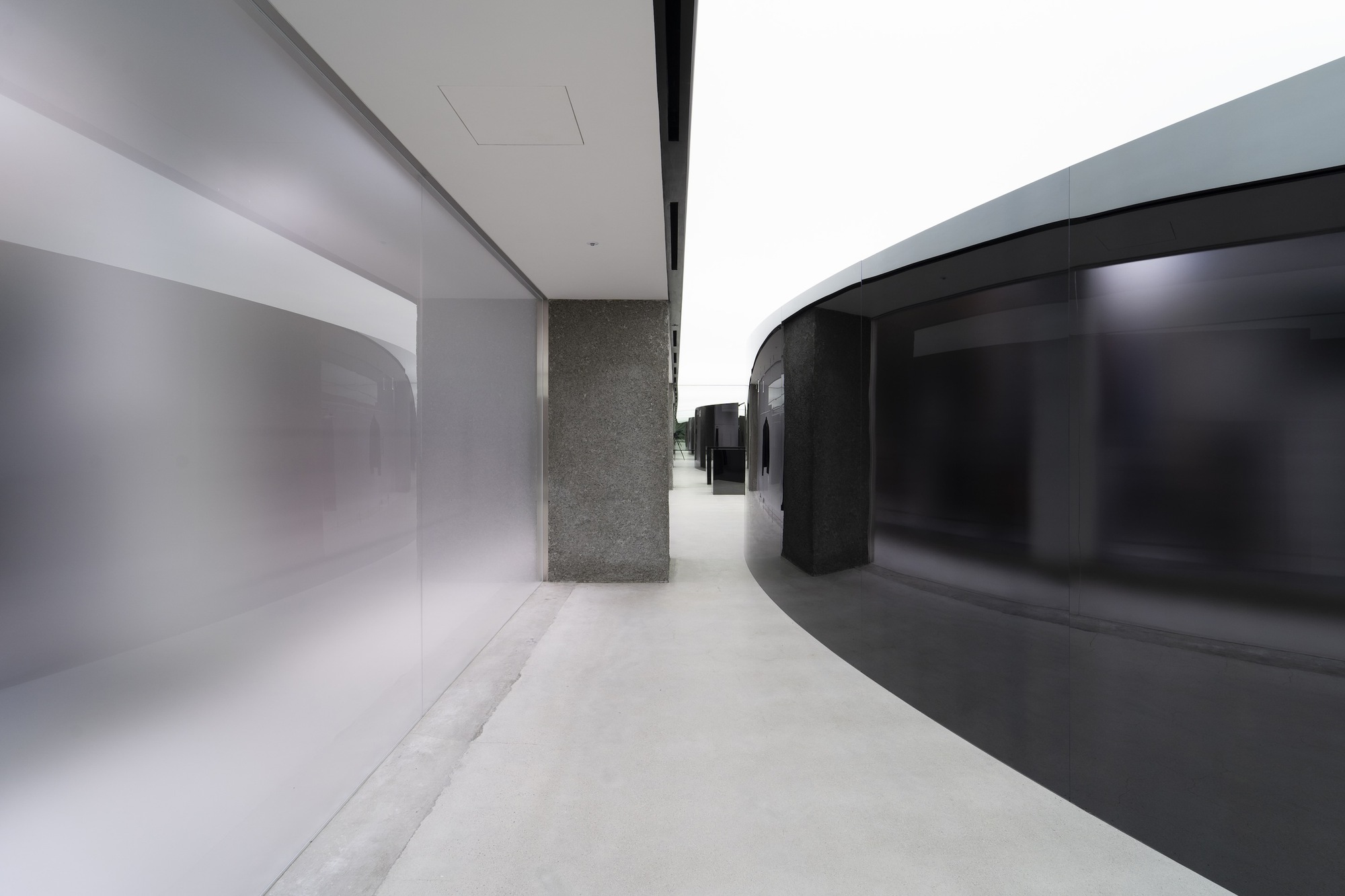 Curved circulation corridor with black glass facade, terrazzo column, and polished white resin floor