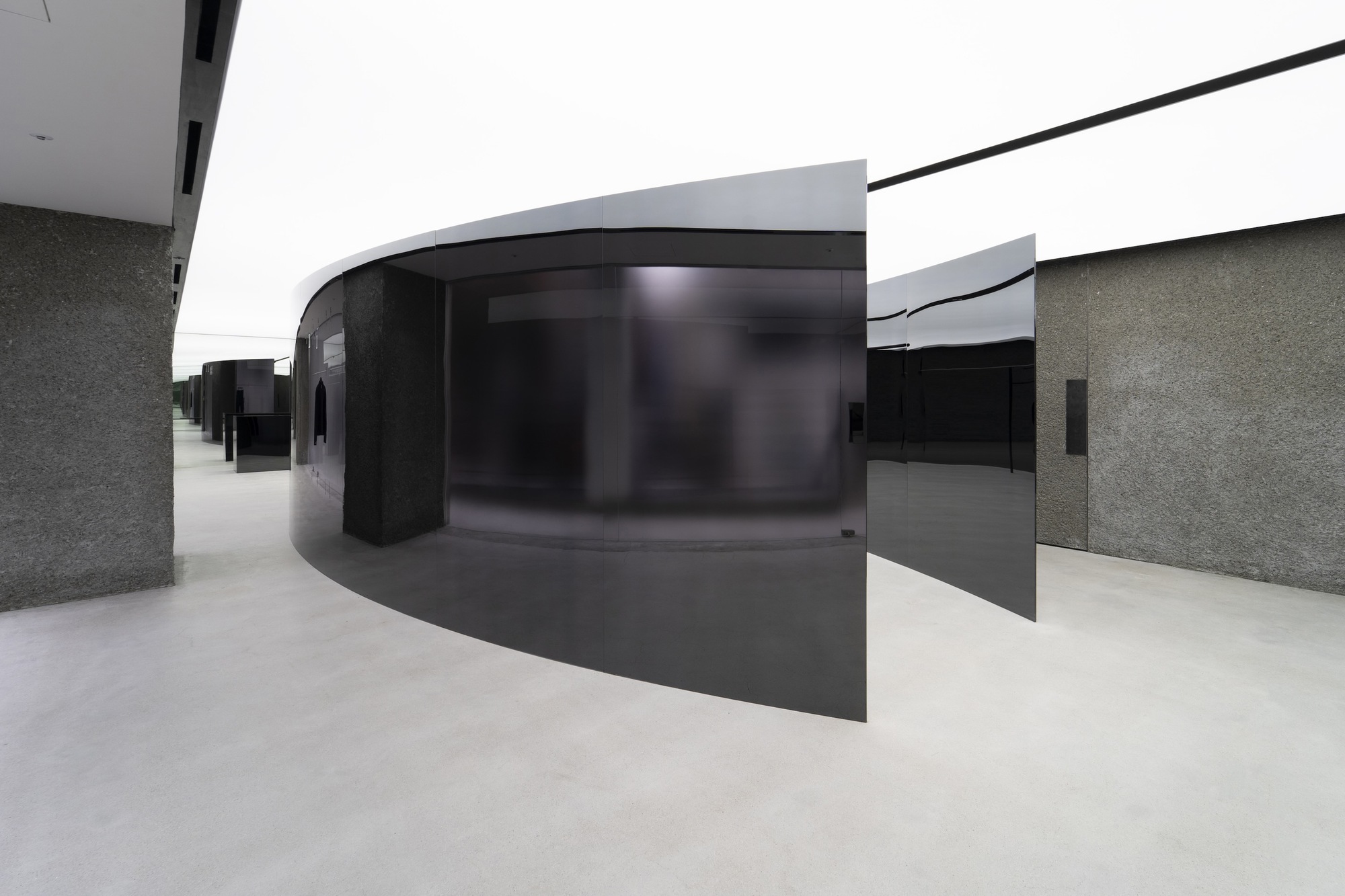 Interior gallery with curved black glass partition and textured grey stone walls under white ceiling planes