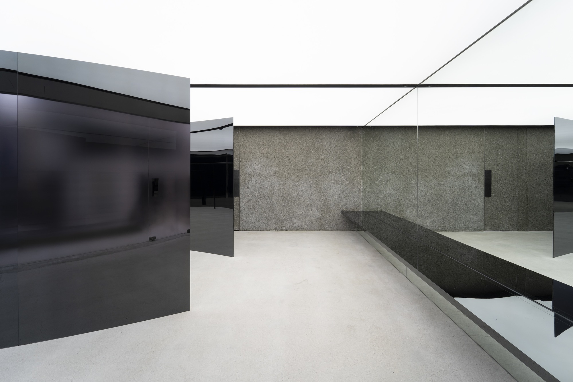 Angular black glass partitions intersecting with textured stone wall and built-in seating bench on polished floor