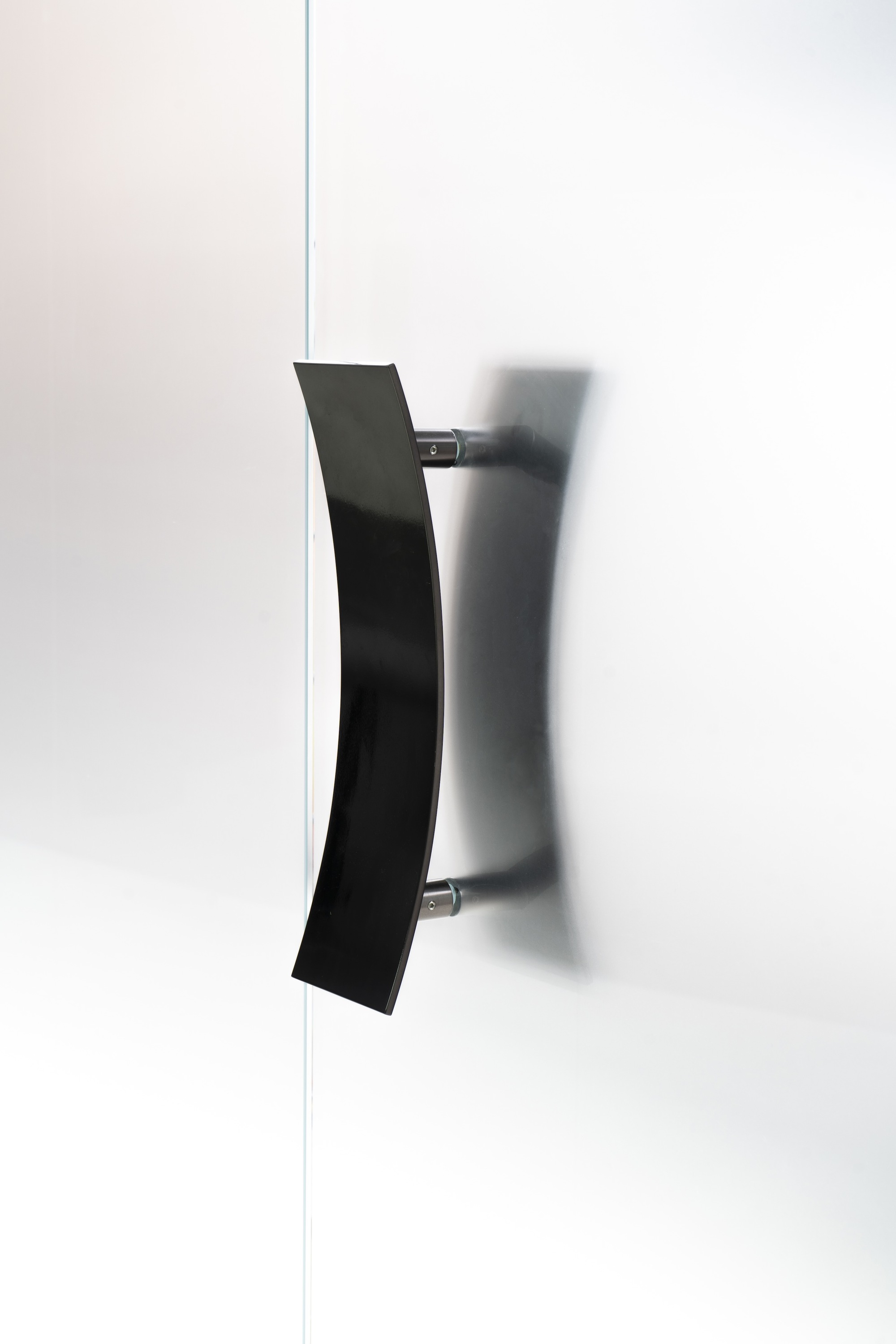 Angled black metal door handle mounted on white wall casting diagonal shadow