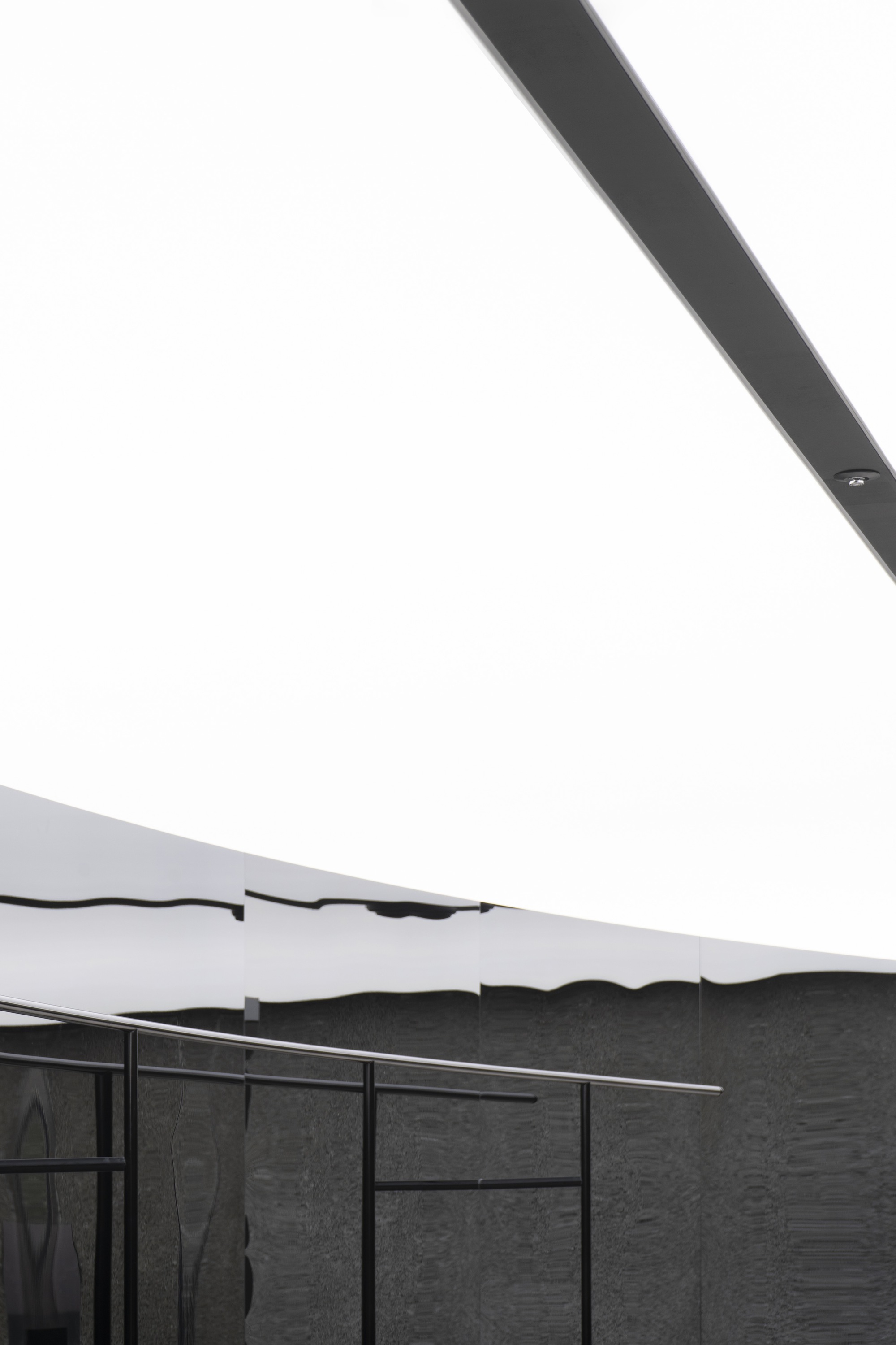 View of undulating white ceiling edge meeting textured dark stone wall with steel-framed glazing below
