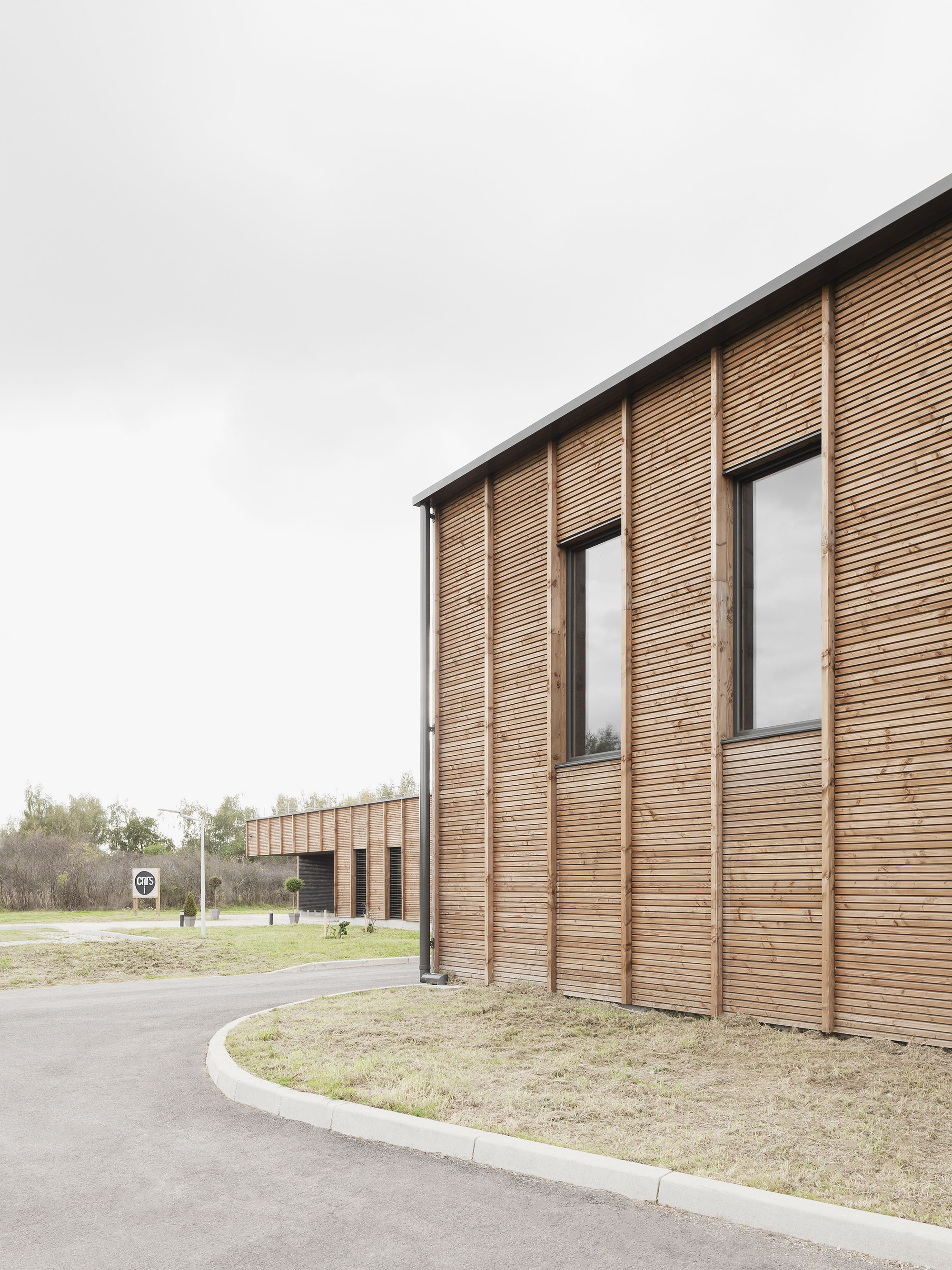 Corner detail of vertical timber cladding with tall narrow windows and curved access road