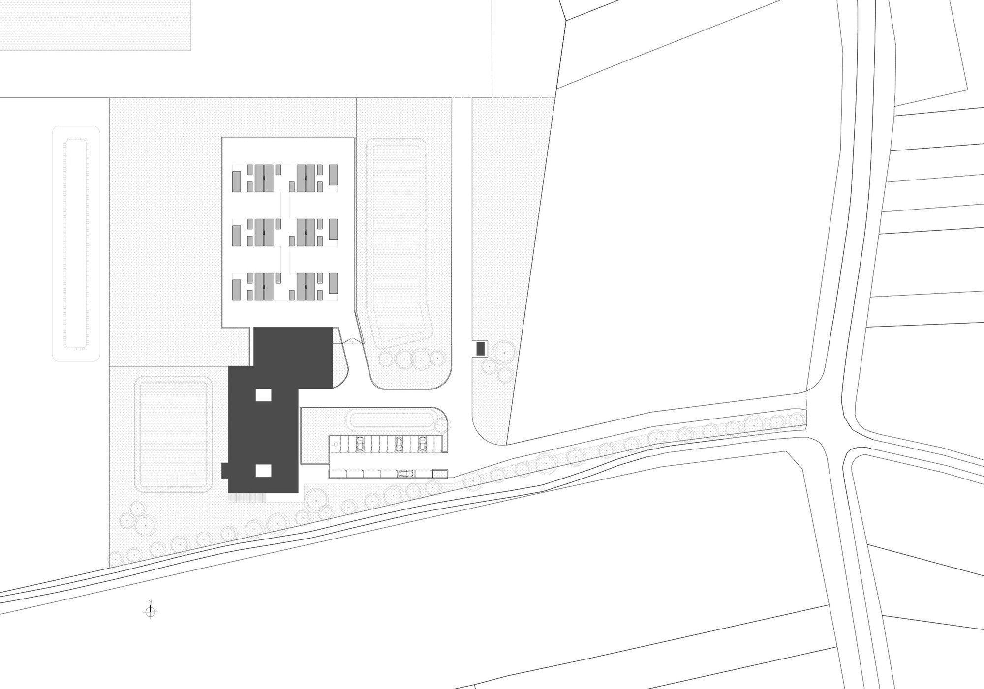 Site plan drawing showing two dark building volumes positioned near a curved roadway and adjacent structures