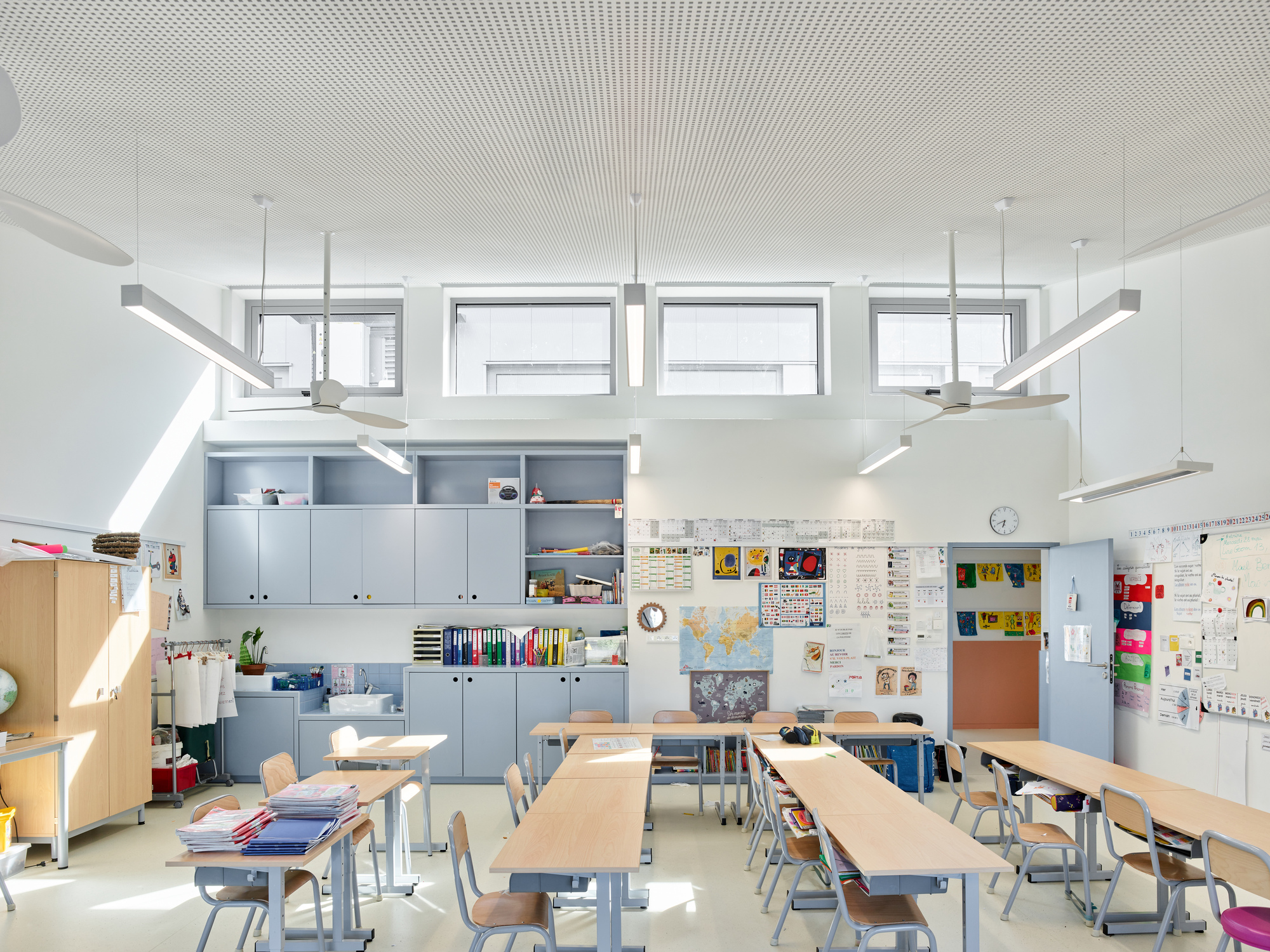 Classroom with perforated ceiling, grey storage units, and timber desks under clerestory glazing