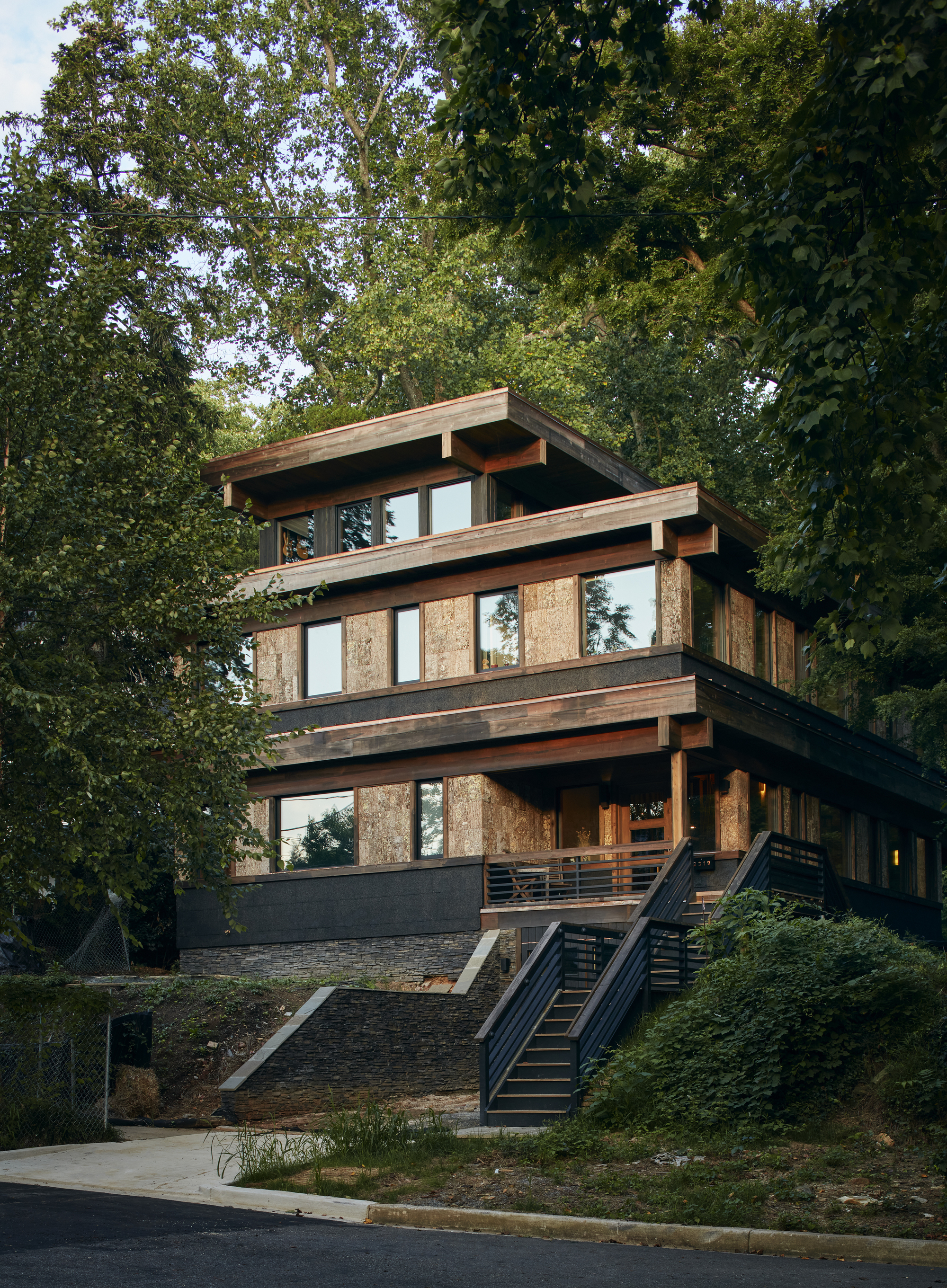 Street-facing facade showing stacked timber-framed volumes with vertical wood panels and a metal exterior staircase