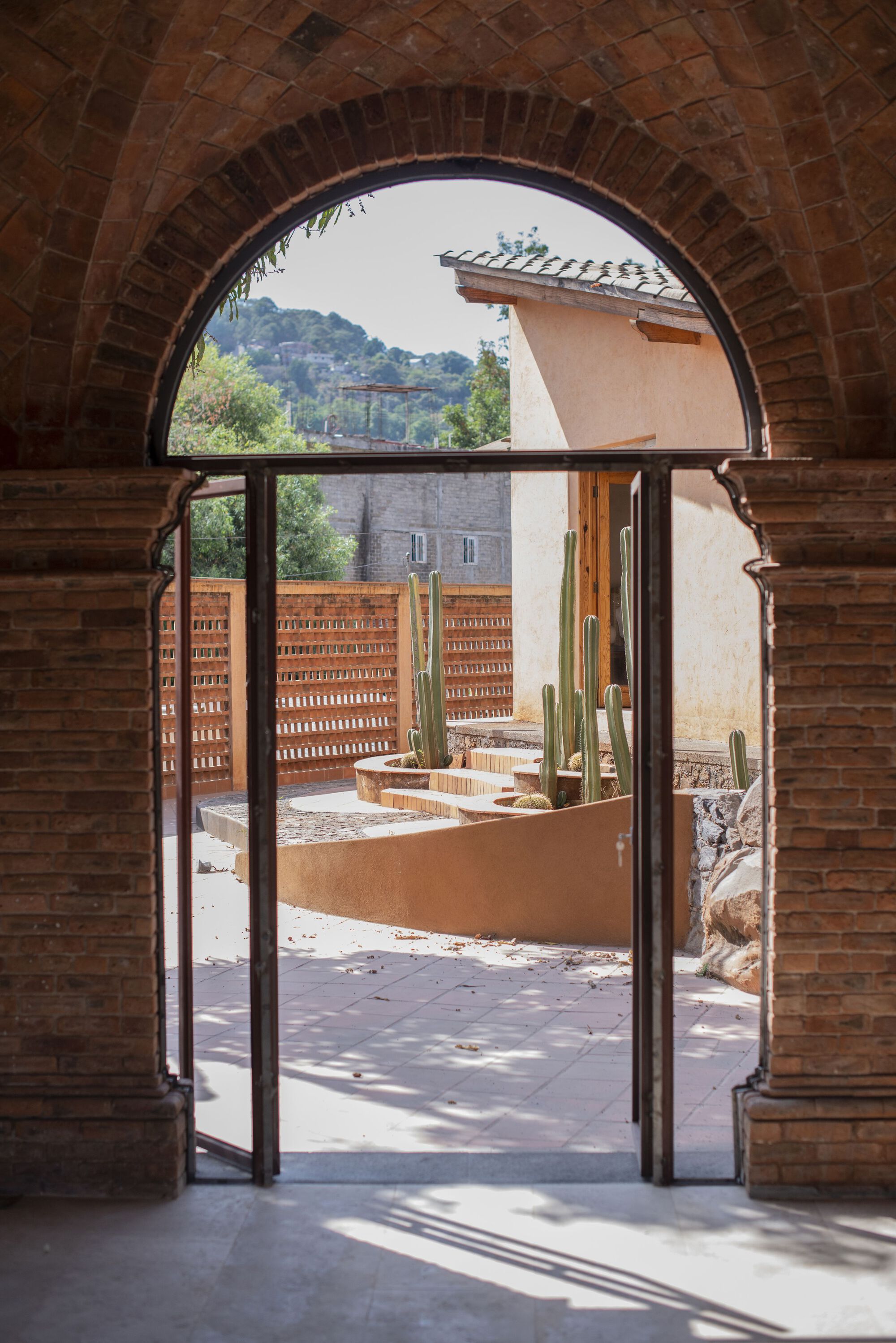 View through an arched brick doorway to a courtyard with planted beds and hills beyond