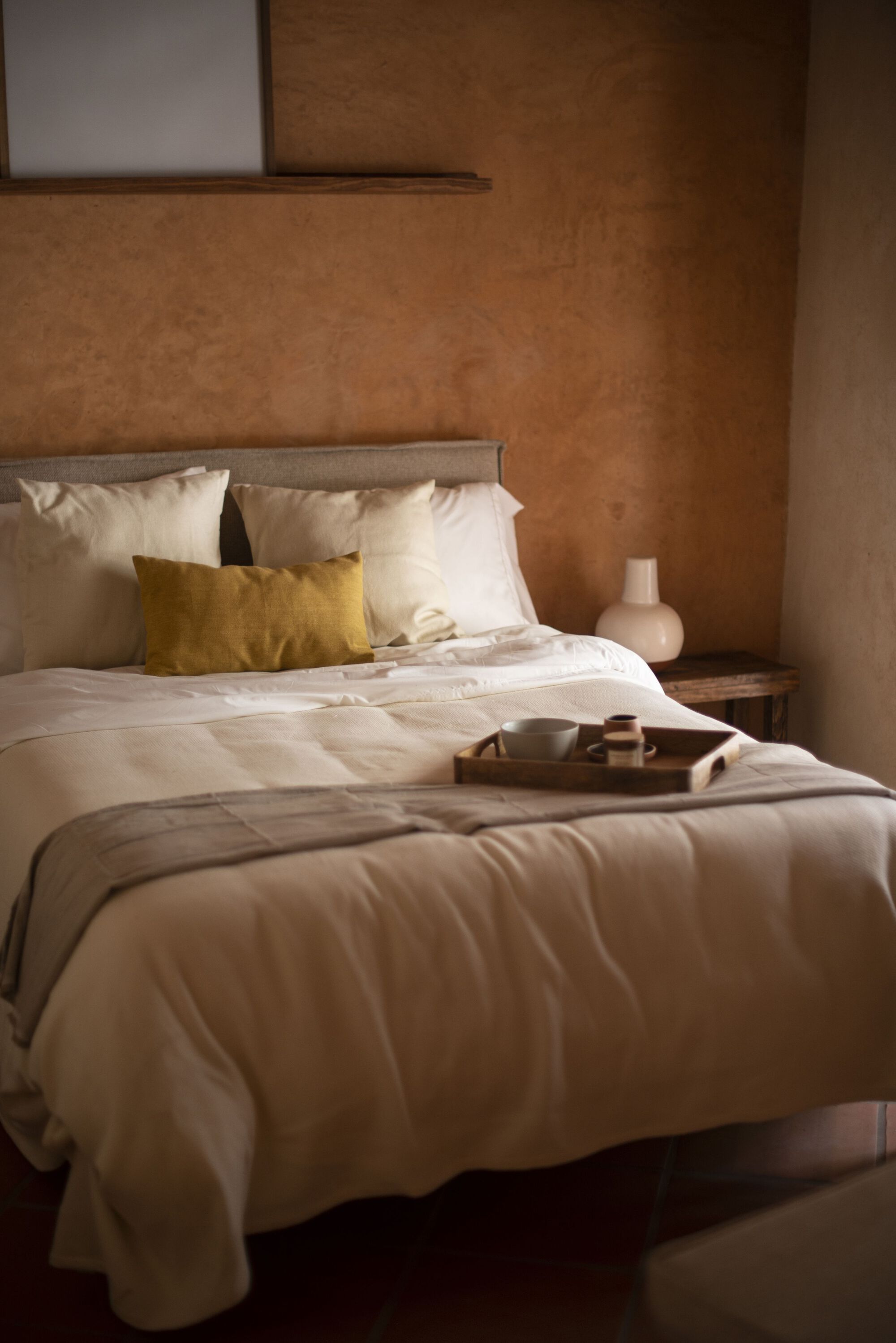 Bedroom with earthen plaster walls and white linens beneath a timber-framed clerestory window