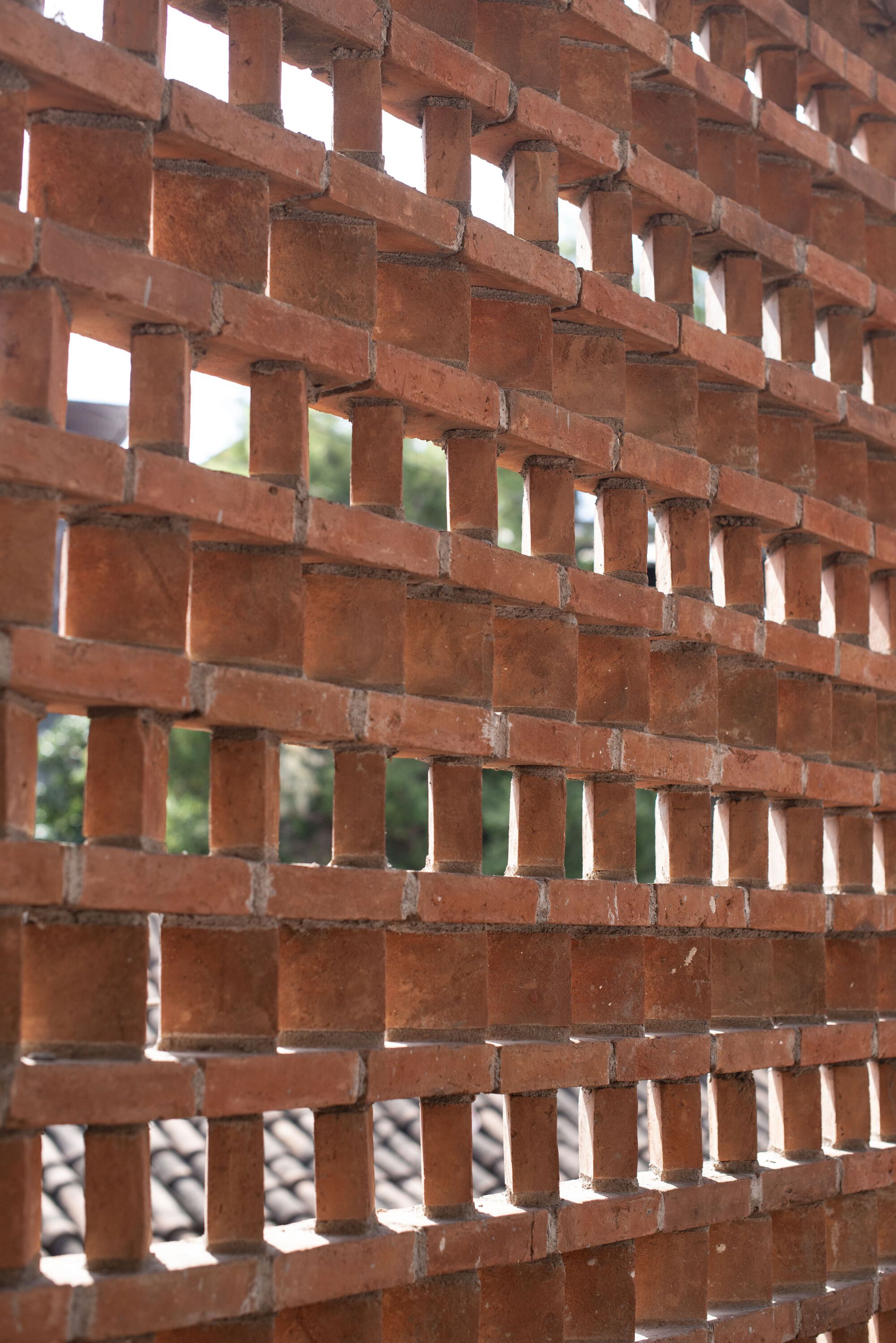 Perforated brick screen wall in running bond pattern filtering daylight and greenery beyond