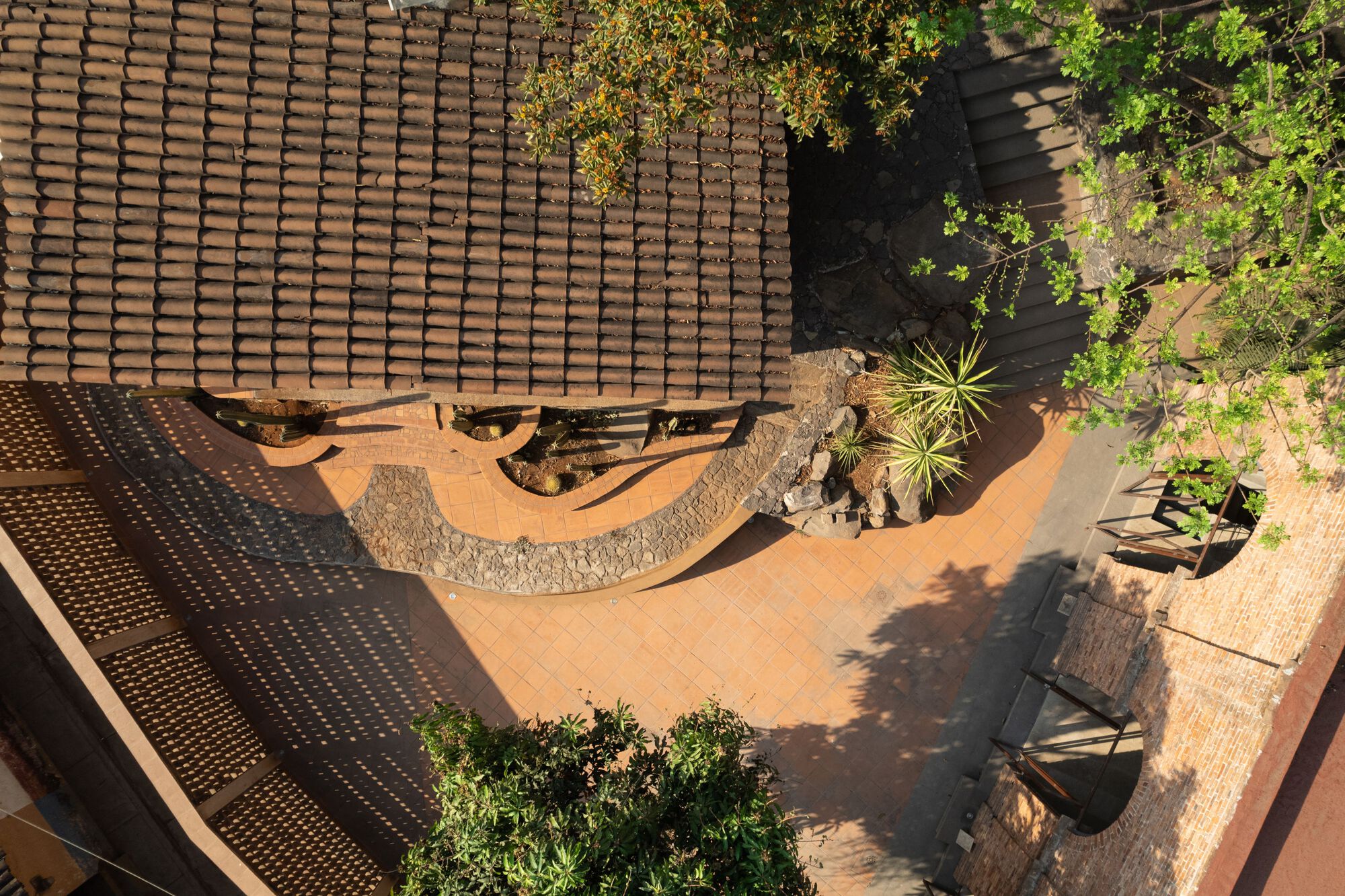 Aerial view of a courtyard with curving stone walls, planted beds and perforated clay roof tiles
