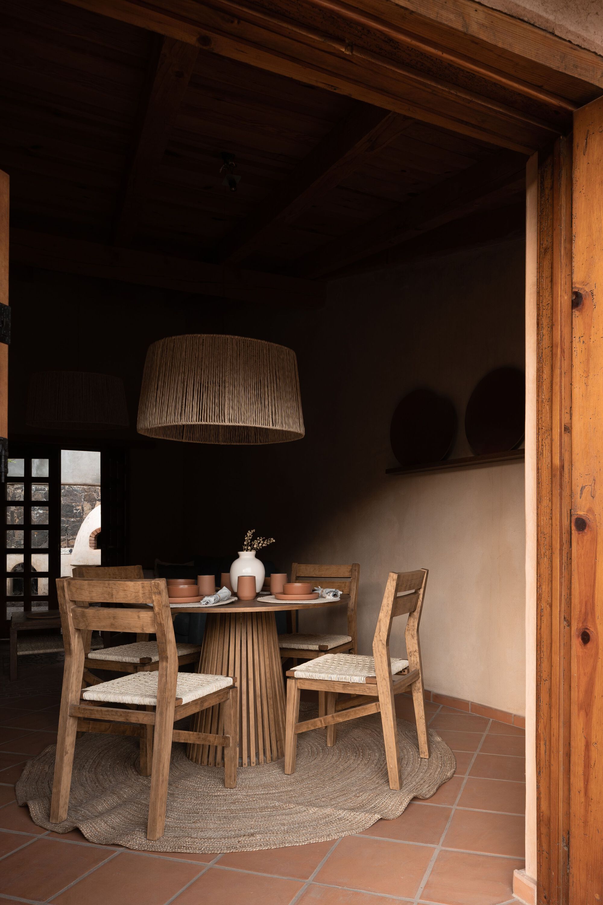 Interior dining area with timber beams, terracotta tile floor and lattice window in dark wall