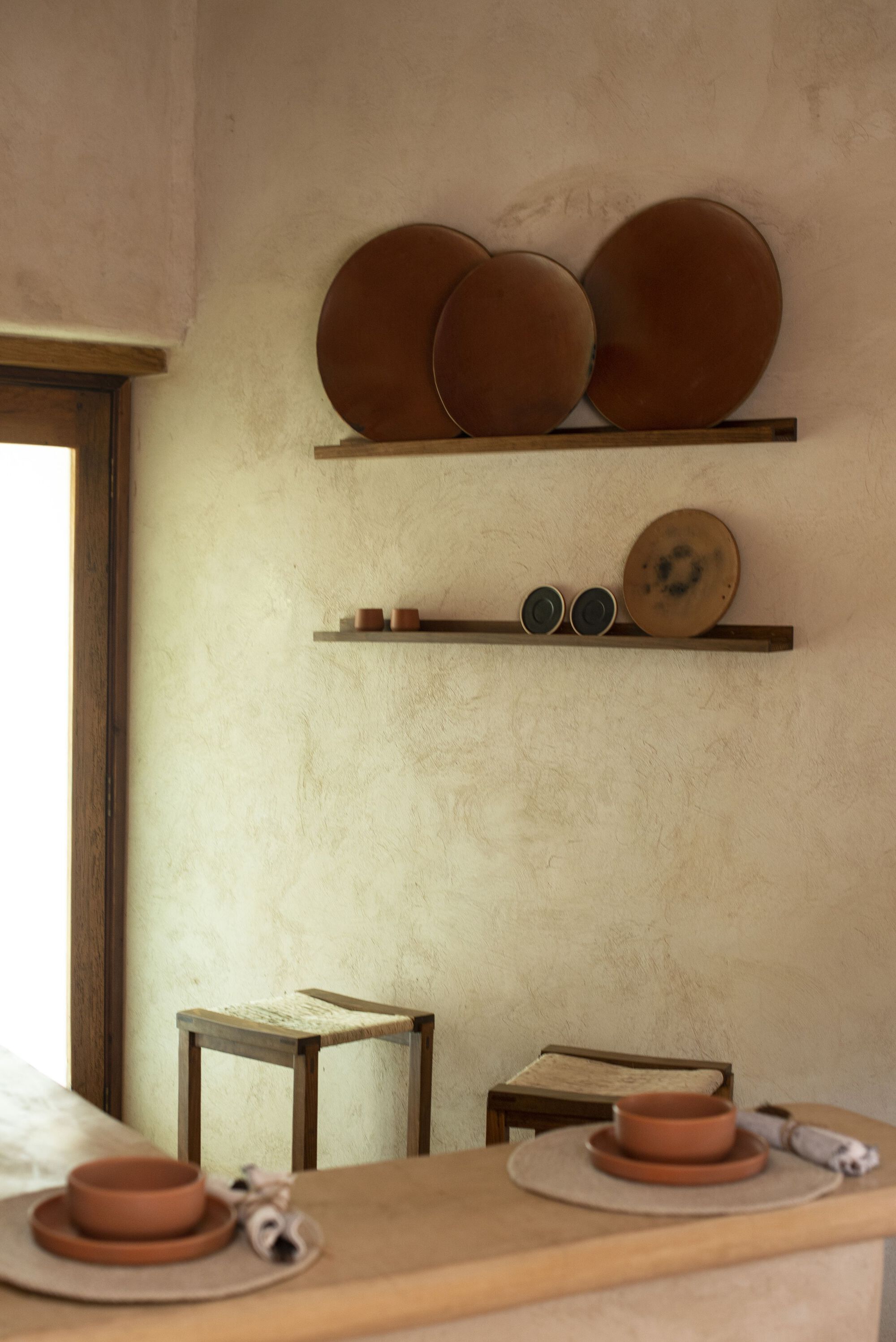 Two floating timber shelves displaying ceramic platters against a textured plaster wall