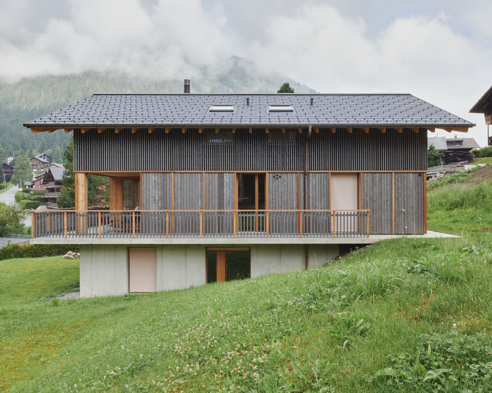 Slate-tiled roof and wooden balcony overlooking a grassy hillside with forested mountains in mist