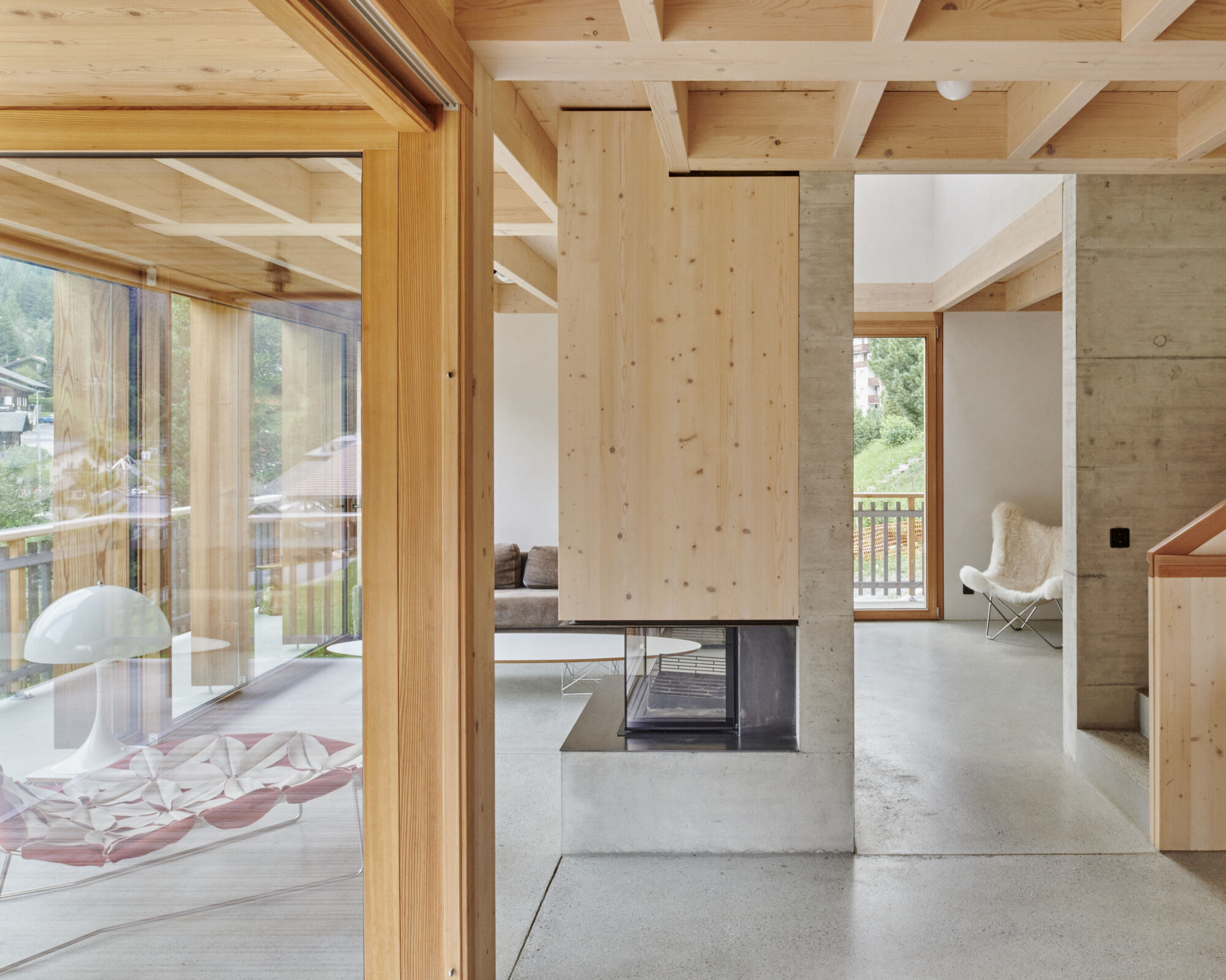 Central concrete fireplace core dividing open living spaces with timber beam ceiling and polished concrete floors