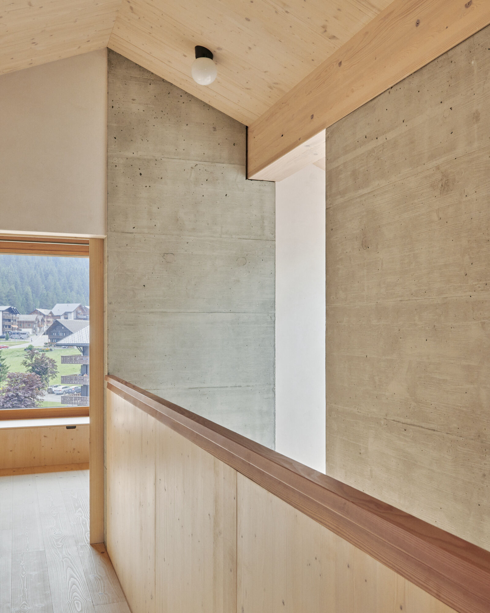 Timber handrail along concrete wall with window overlooking valley and village below