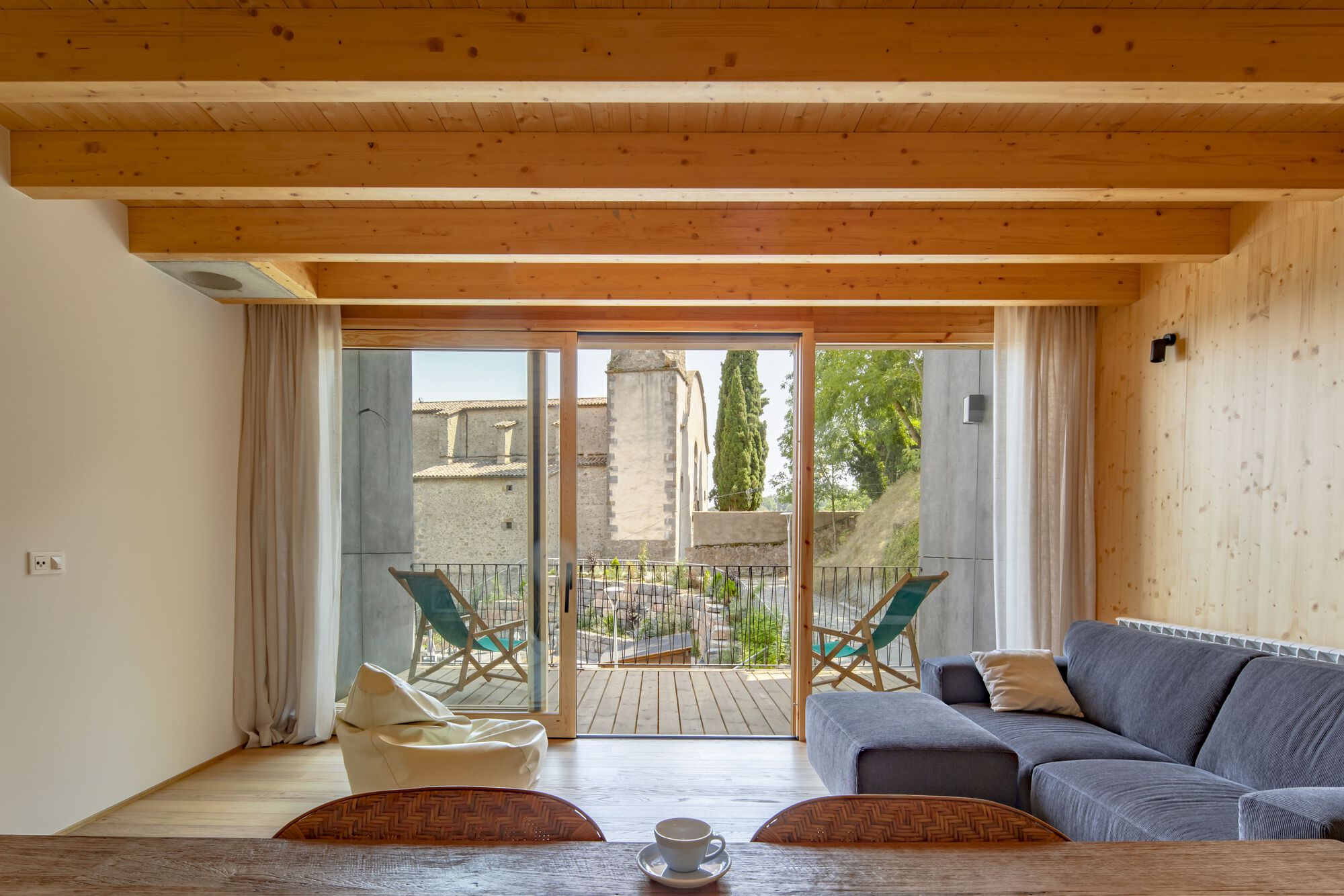 Living room with exposed timber beams and glazed doors opening to a balcony with two lounge chairs