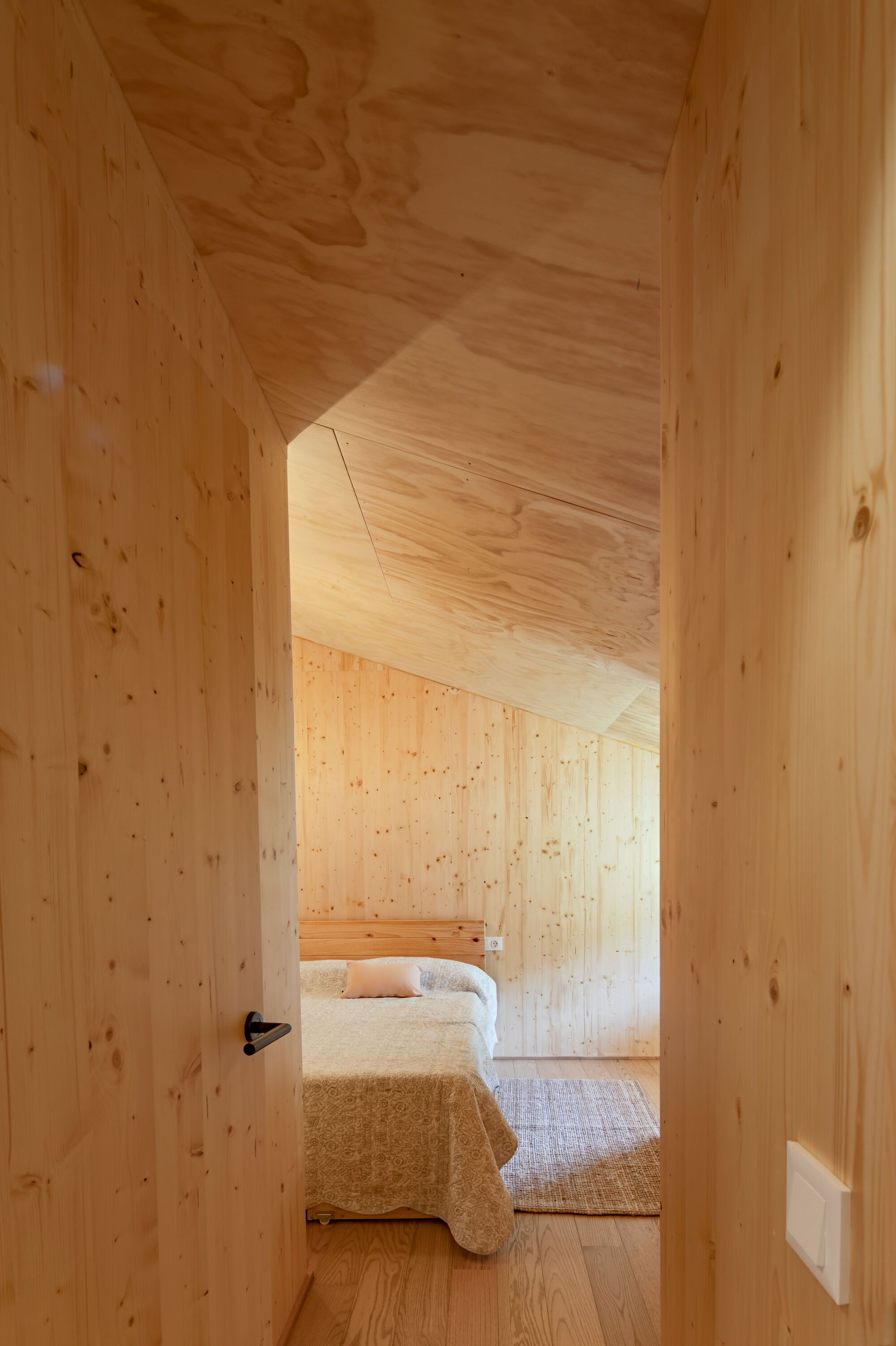 Timber-lined corridor leading through an angled doorway to a bedroom with natural daylight