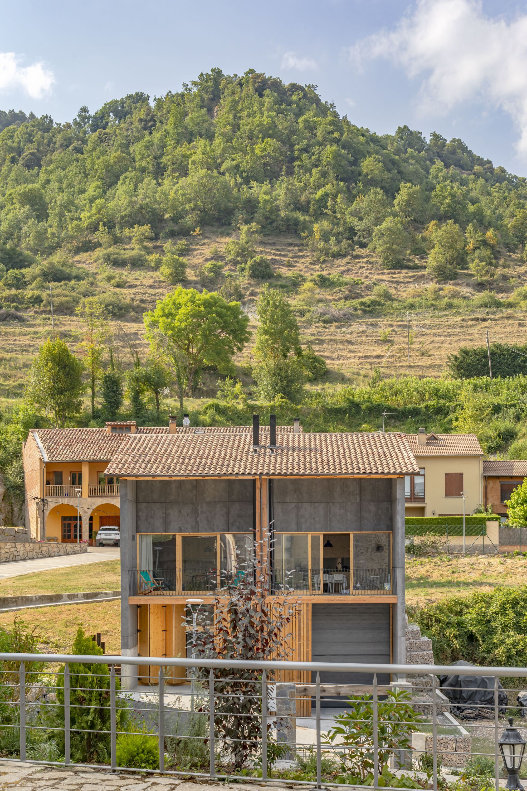 Concrete and timber house with exposed rafters beneath a terraced hillside planted with trees