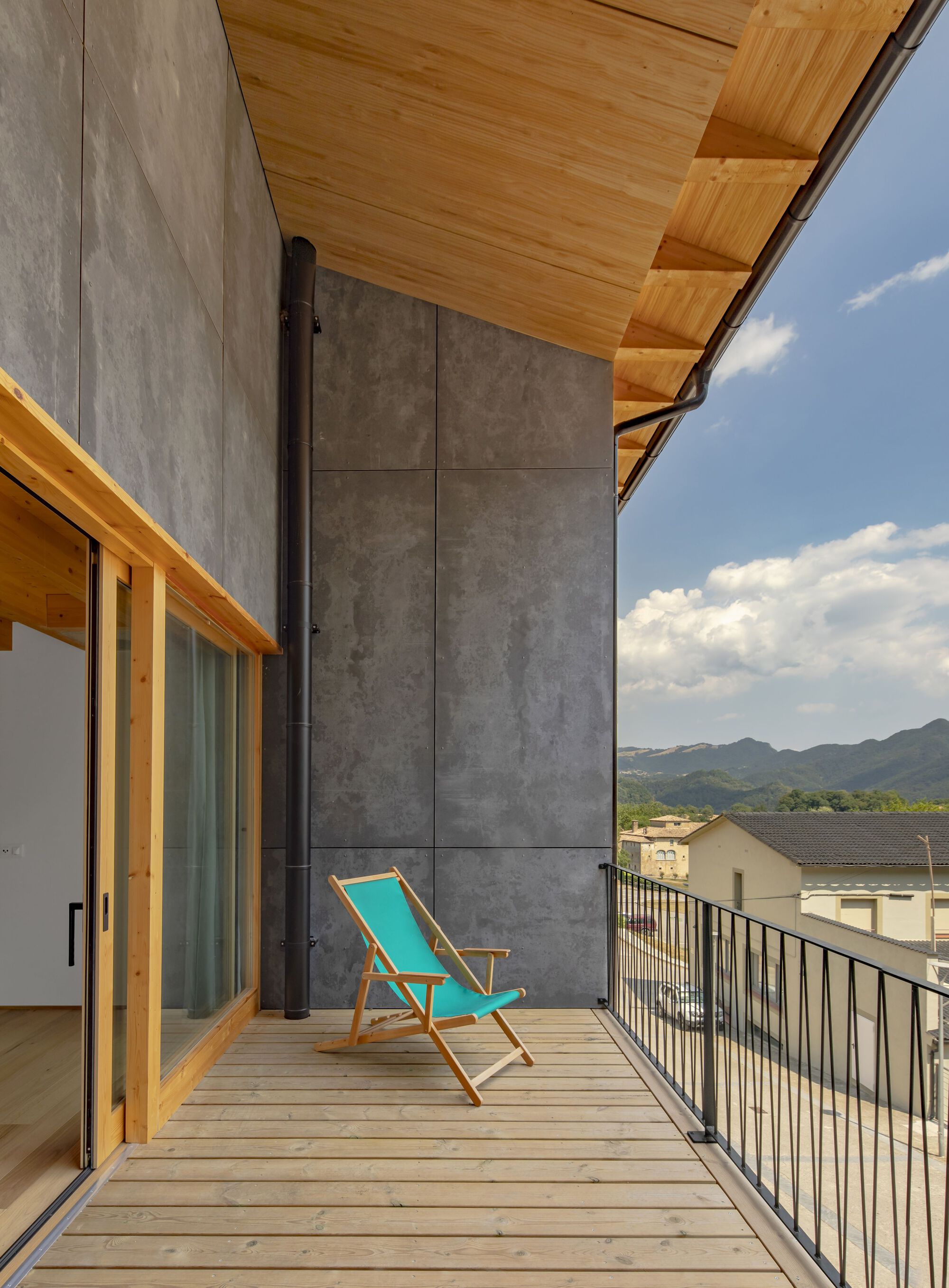 Timber deck balcony with metal railing and turquoise chair looking toward distant mountains