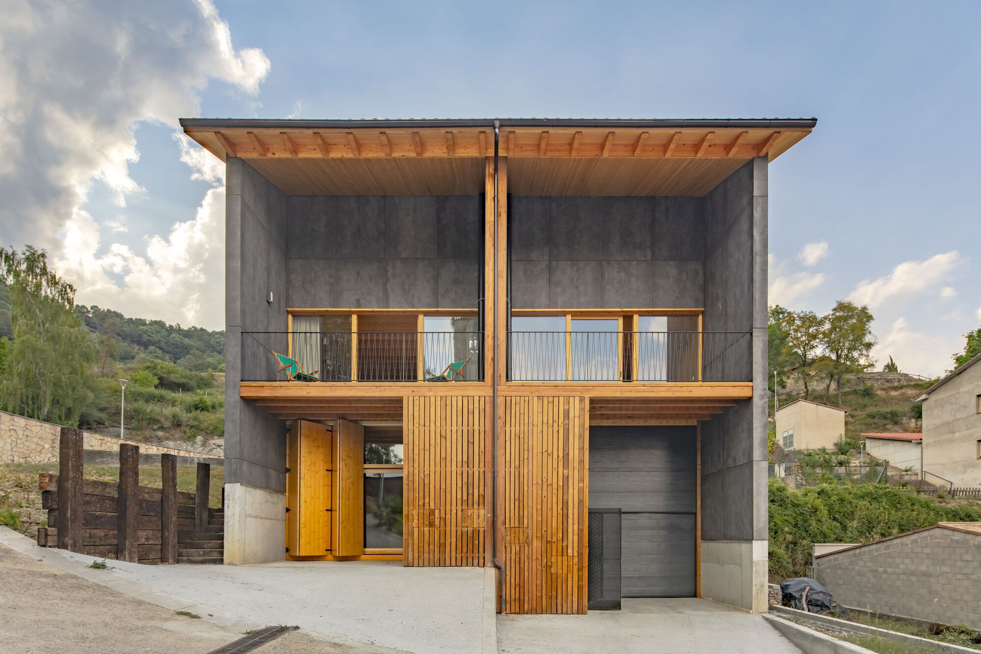 Street facade with vertical timber slats flanking a garage door beneath concrete panels and timber eaves