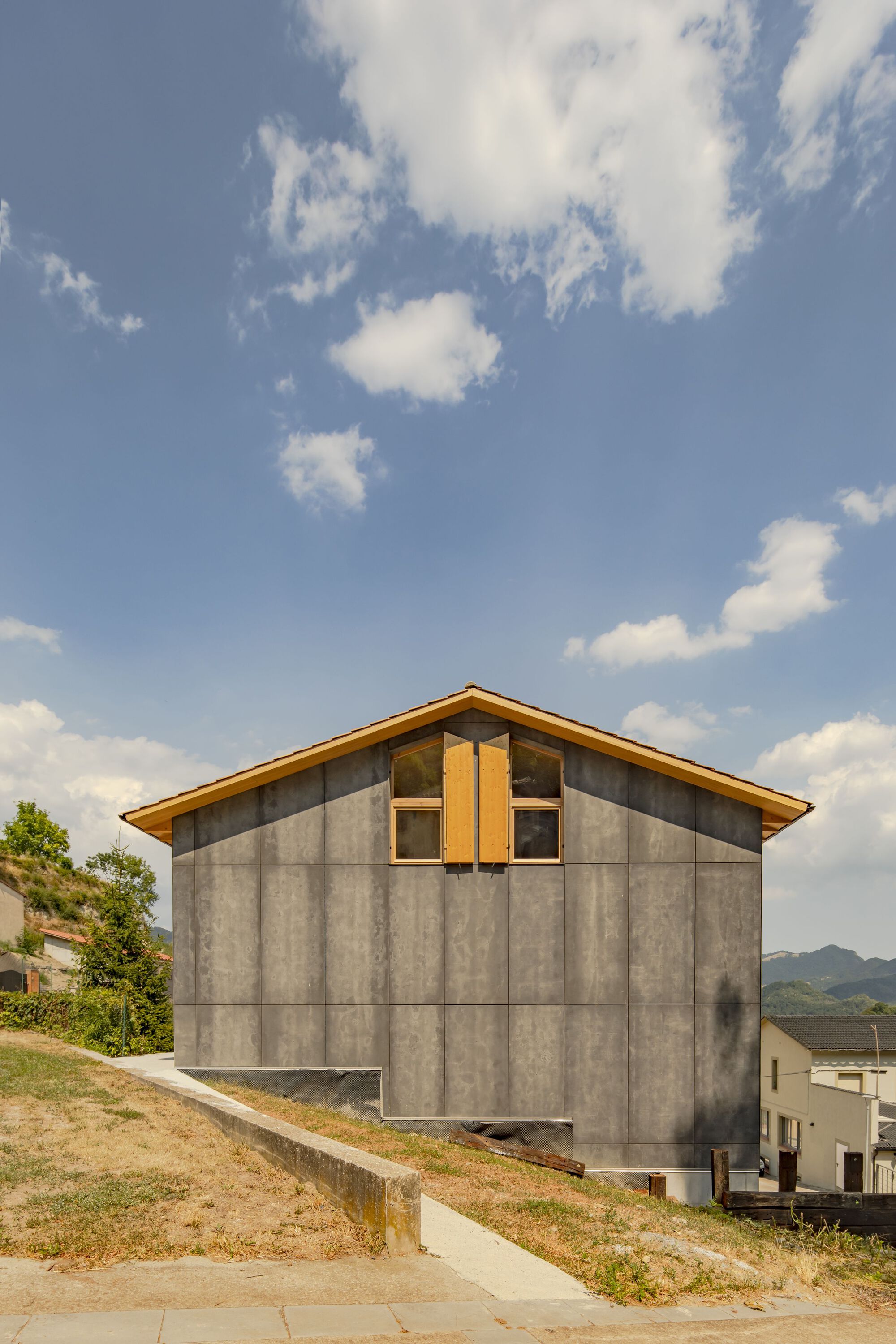 Gable end showing large-format concrete panels with timber trim window beneath a cloudy sky