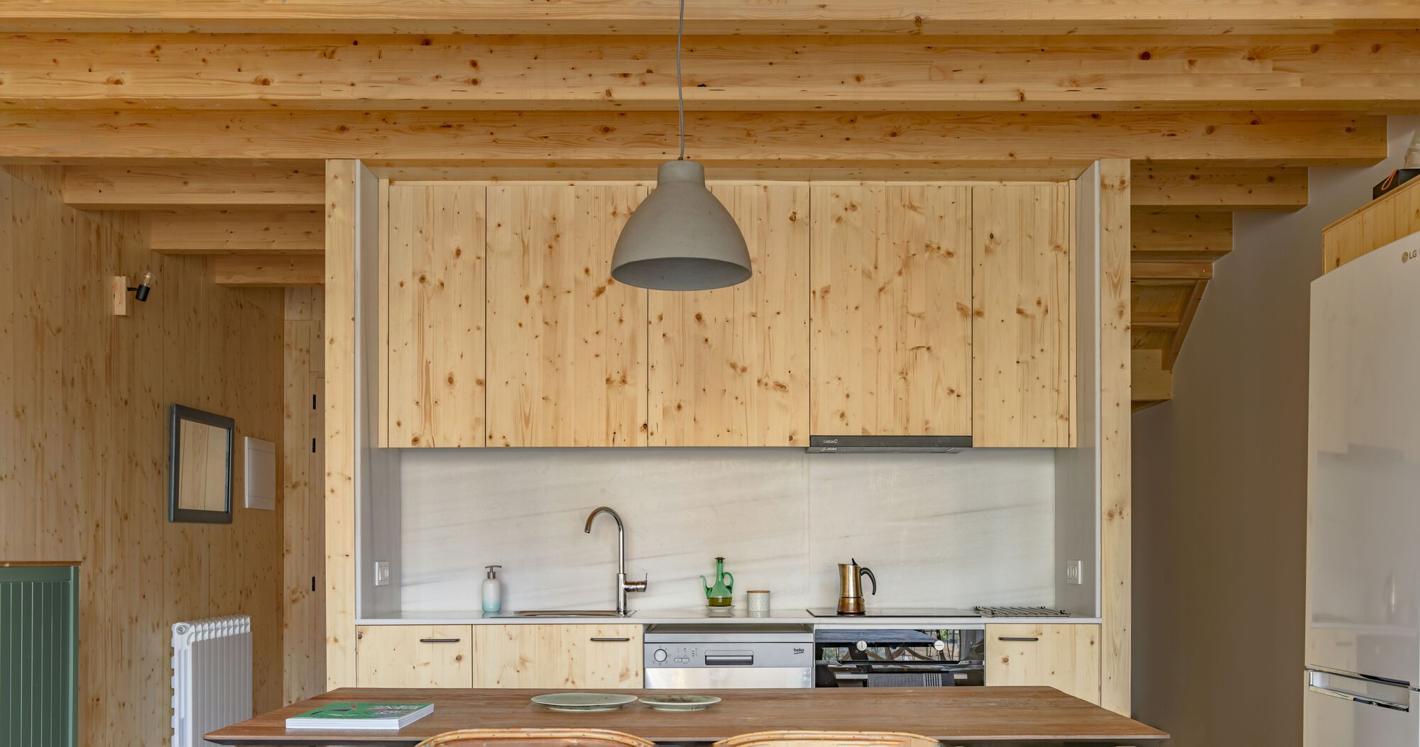 Kitchen with pale wood cabinetry, exposed timber ceiling beams and a grey pendant light