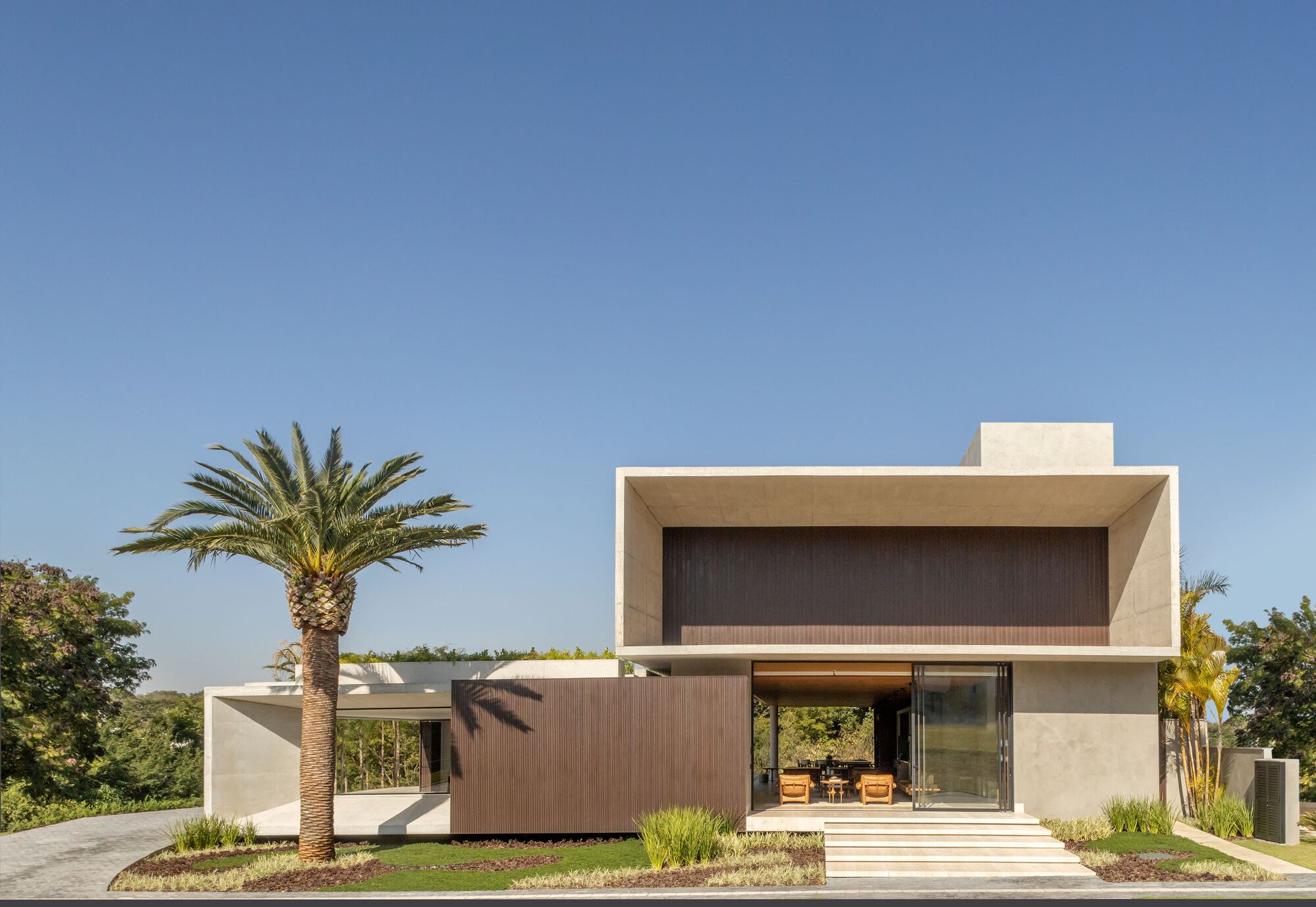 Front facade with cantilevered concrete volumes and timber-clad screens framed by a palm tree