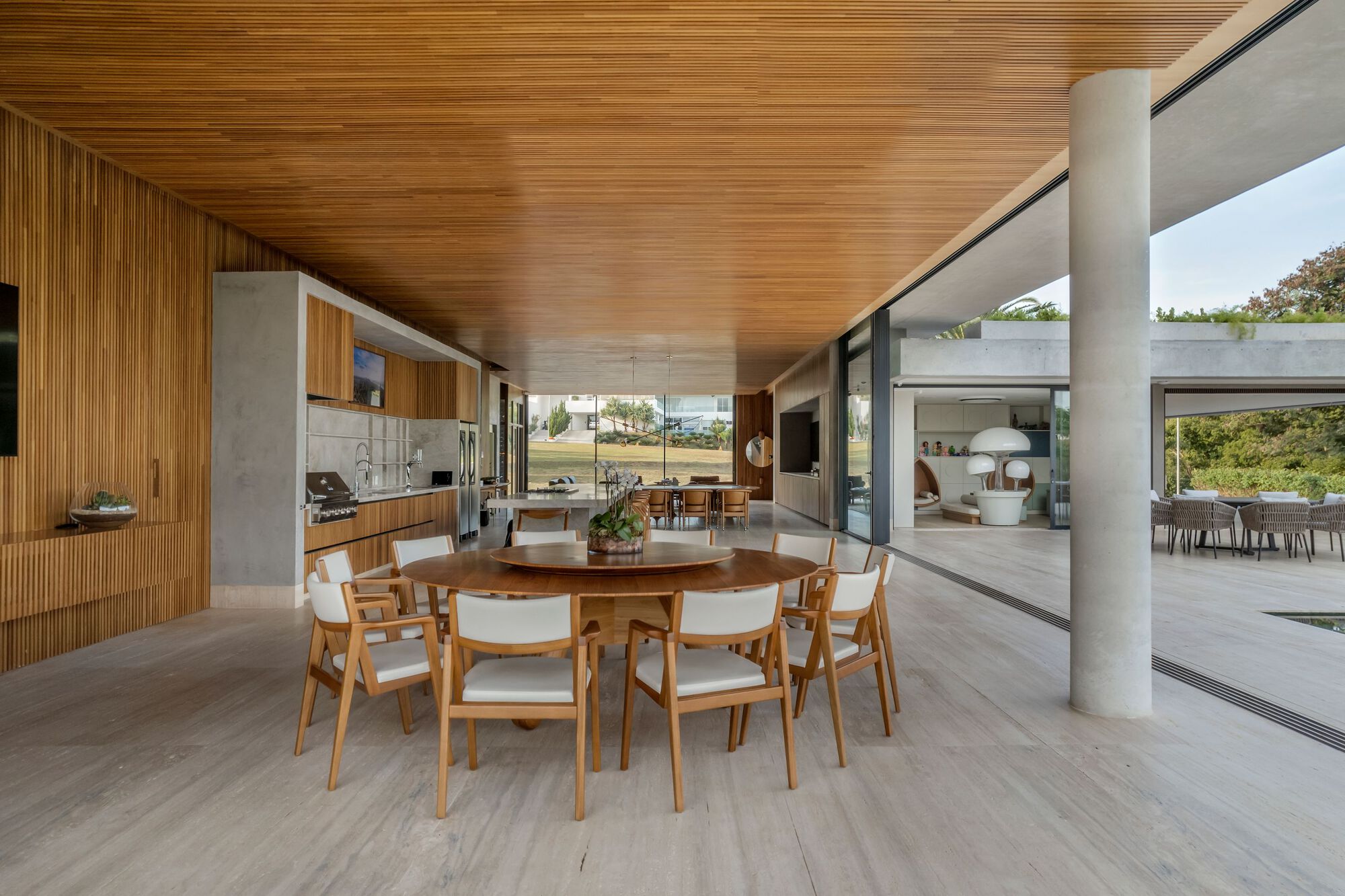 Open-plan living space with timber slatted ceiling and cylindrical concrete columns framing views to landscape