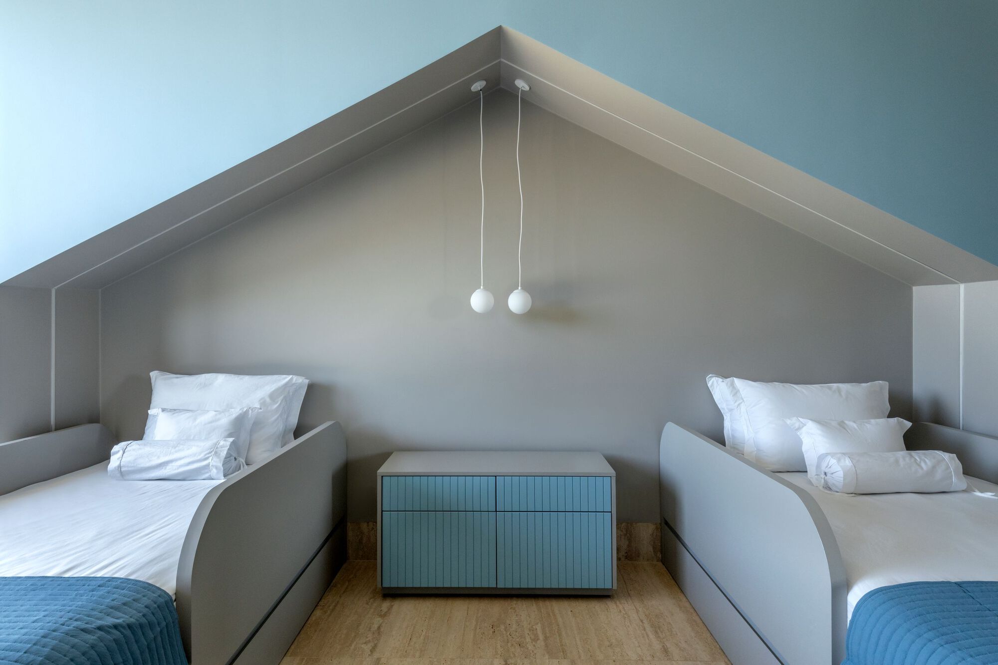 Attic bedroom with two beds under sloped white ceiling and suspended pendant lights