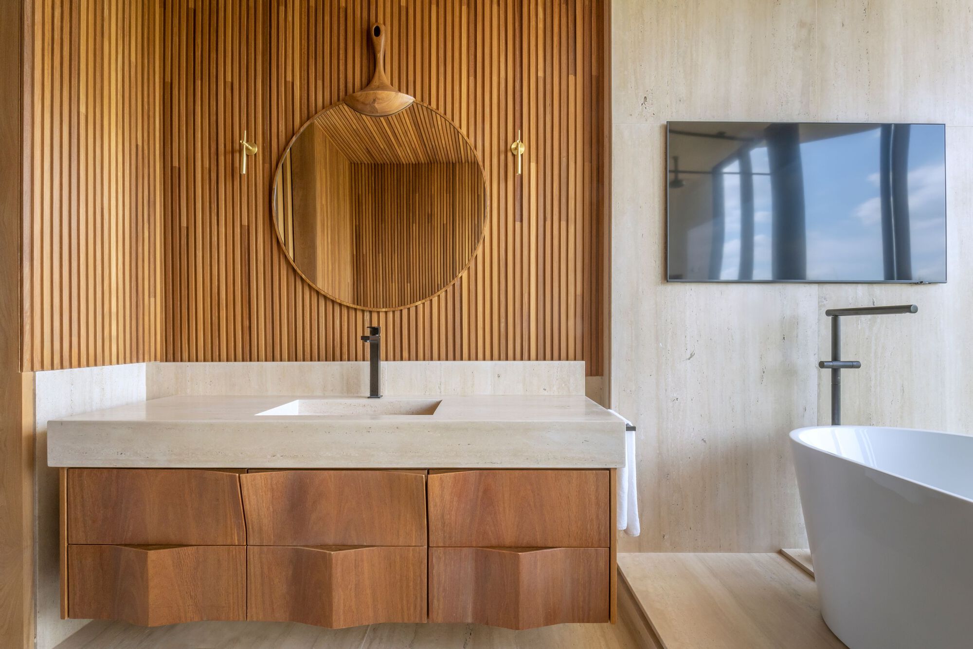 Floating vanity with integrated sink below a round mirror against vertical wood slat wall