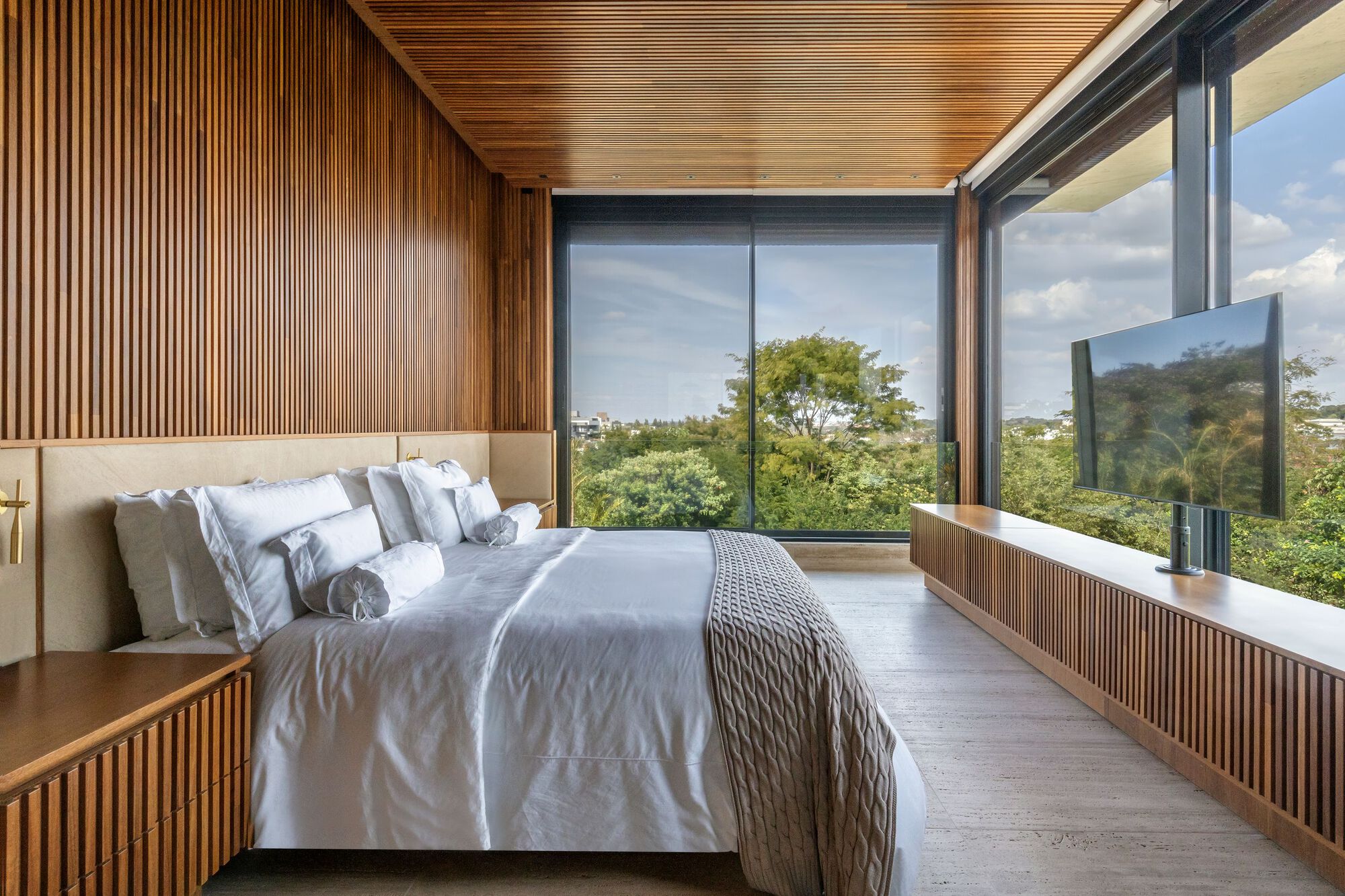 Bedroom with floor-to-ceiling windows framing green hillside under a slatted wood ceiling