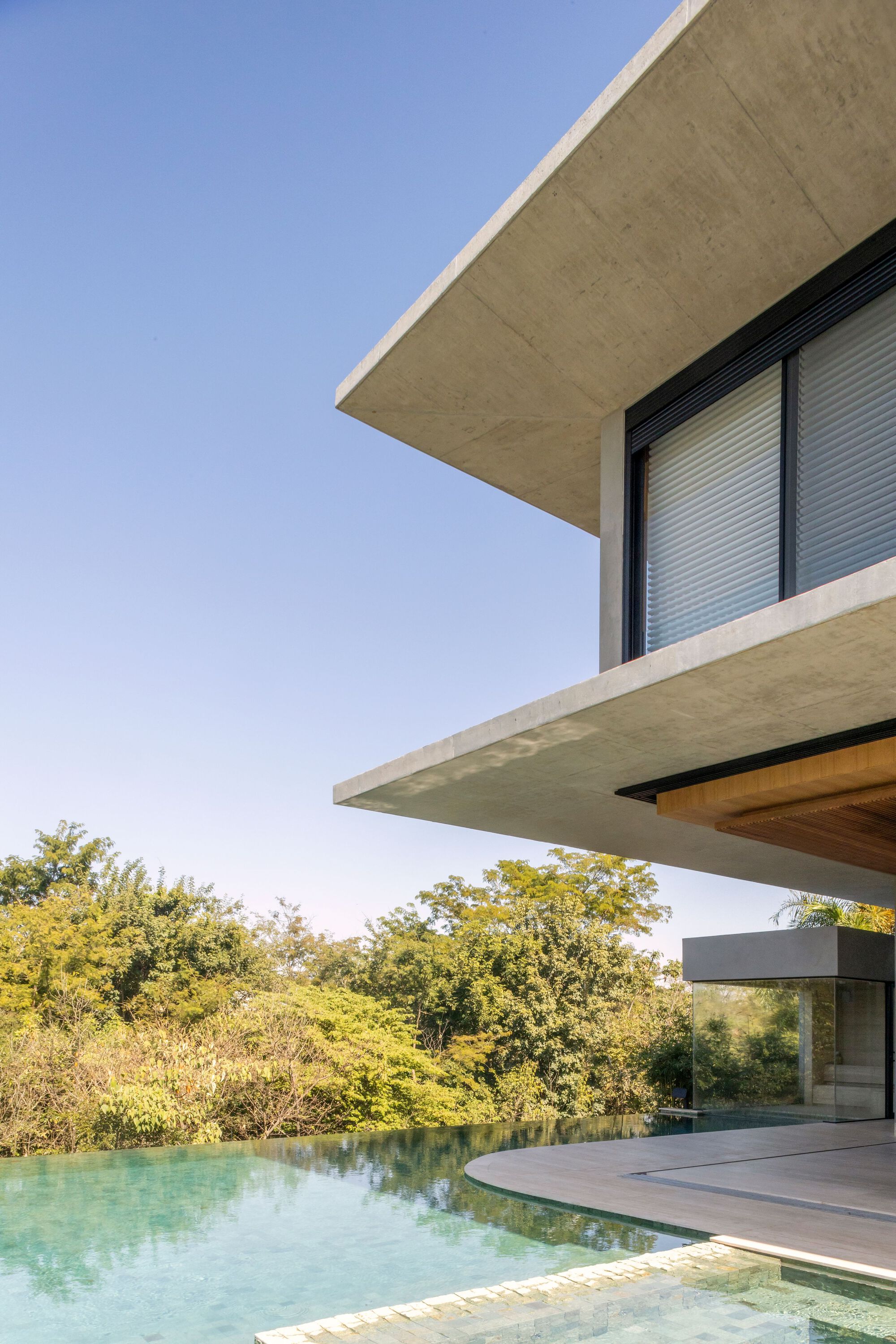 Cantilevered concrete terrace with shutter-clad window above infinity pool and surrounding trees
