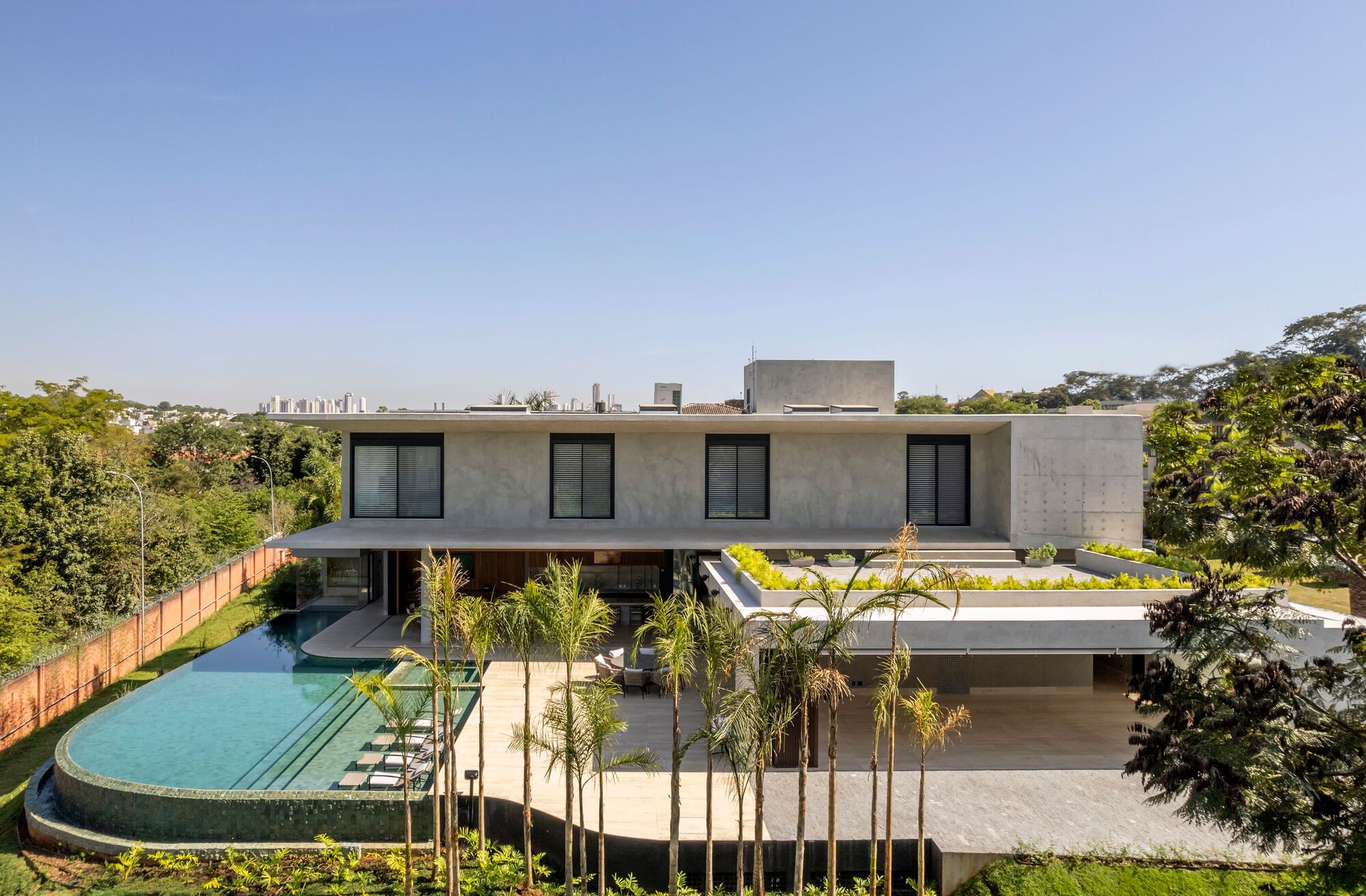 Concrete volume residence with cantilevered roof plane above curved pool and young palm plantings